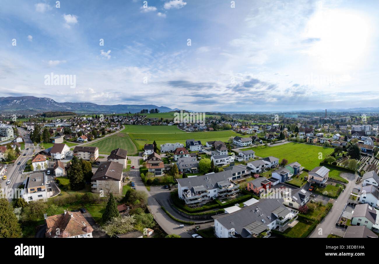 Luftaufnahme von Wohnhäusern, grünen Wiesen und fernen Bergen unter hellem Himmel in Biberist, Solothurn, Schweiz. Stockfoto