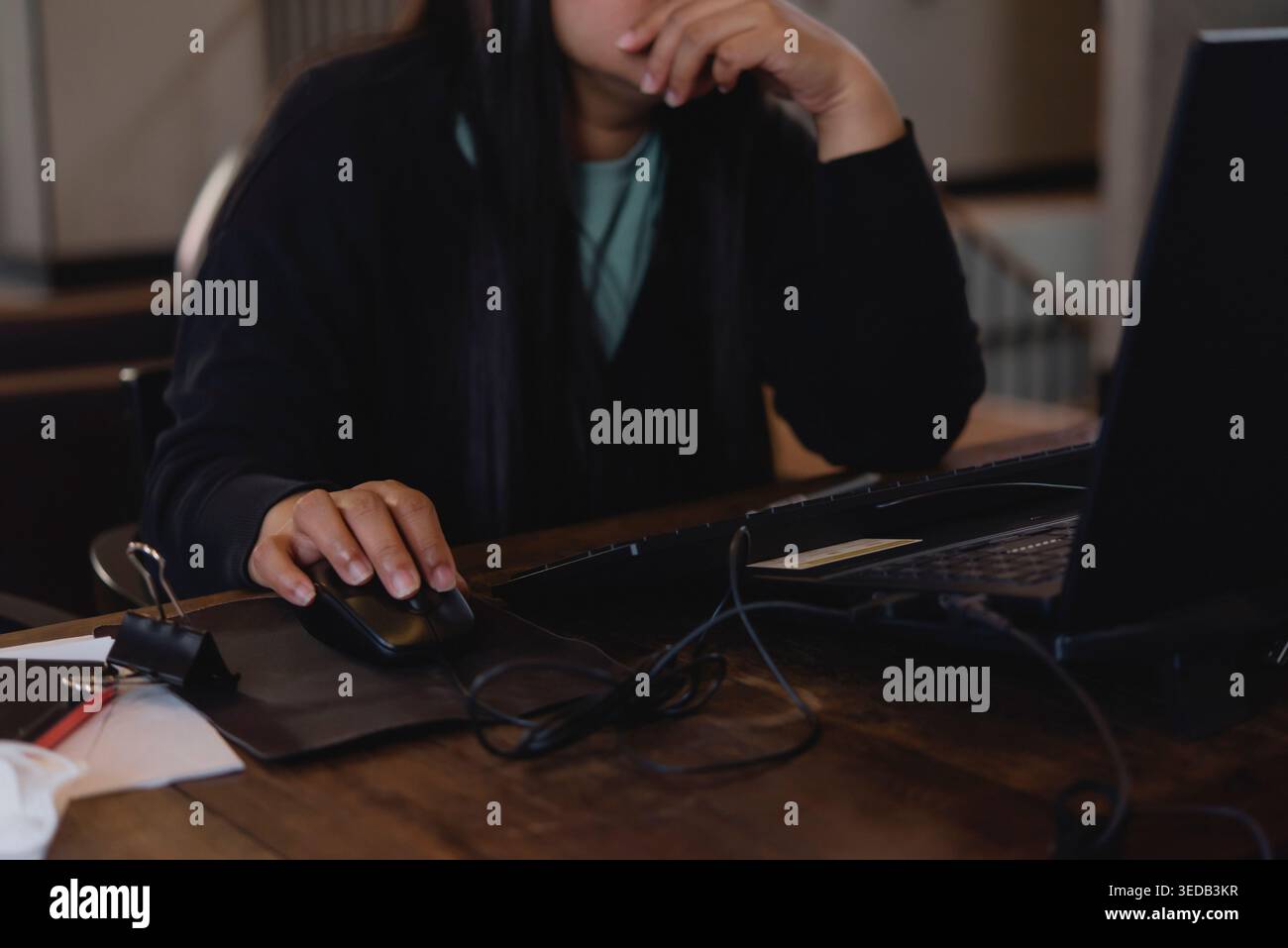 Gestresste Frau, die mit der Hand am Kinn am Laptop arbeitet. Ernsthafte weibliche Person mit Computermaus, die über Probleme oder Cybermobbing-Konzept nachdenkt. Stockfoto