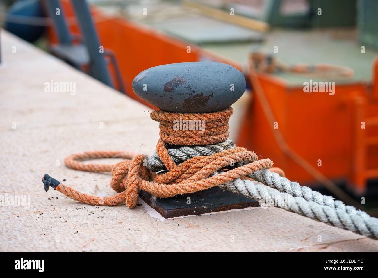 Nahaufnahme von Festmacherseilen, die um Metallpfoller auf dem Bootsdeck gebunden sind, nautische Details mit verschwommenem Yachthafen-Hintergrund, Seeverkehrskonzept Stockfoto