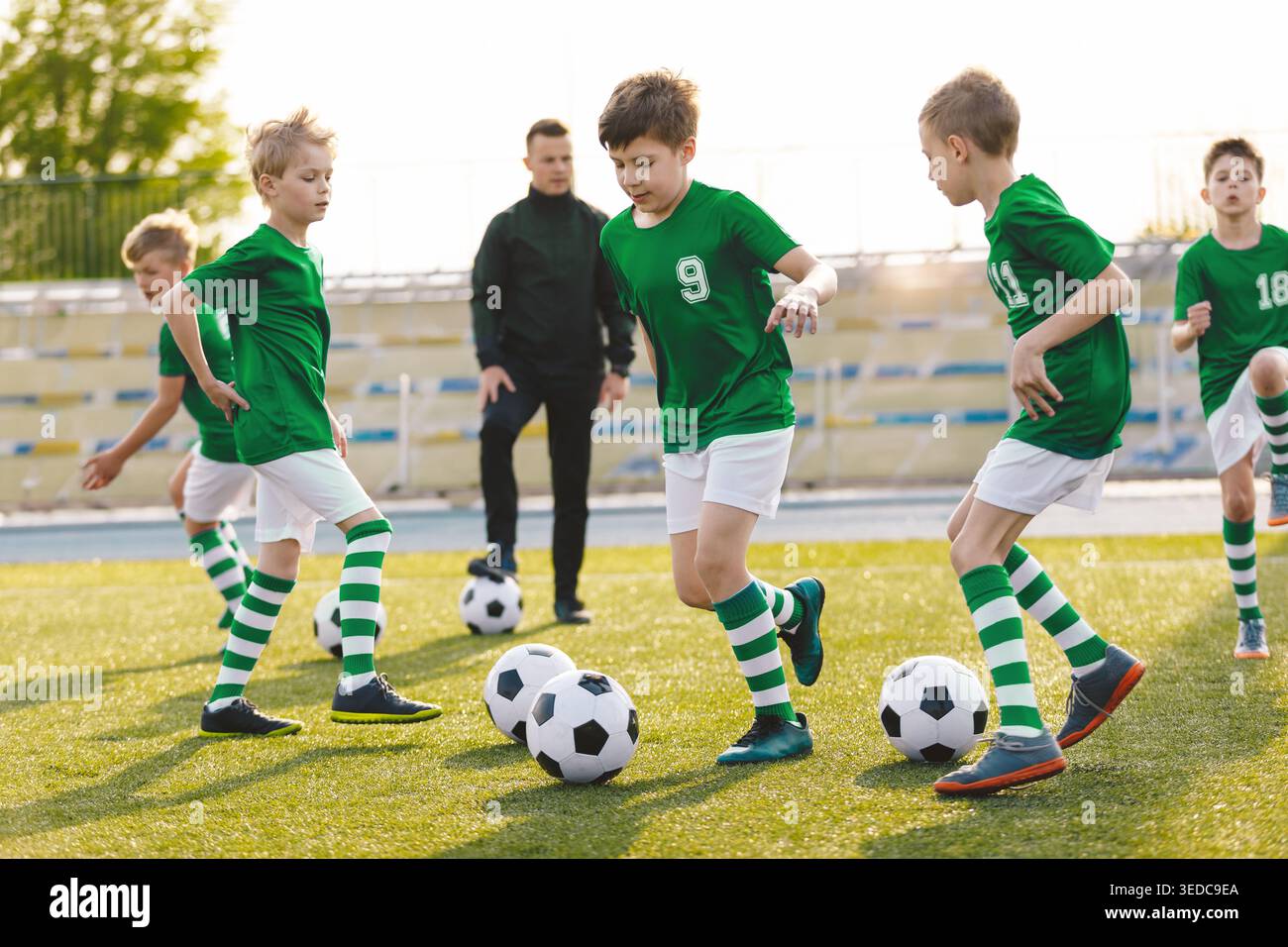 Jugendfußballmannschaft in grünen Uniformen, die Übungen mit Trainer auf Sunny Grass Field üben - Junior Football Training und Spielerentwicklung Stockfoto
