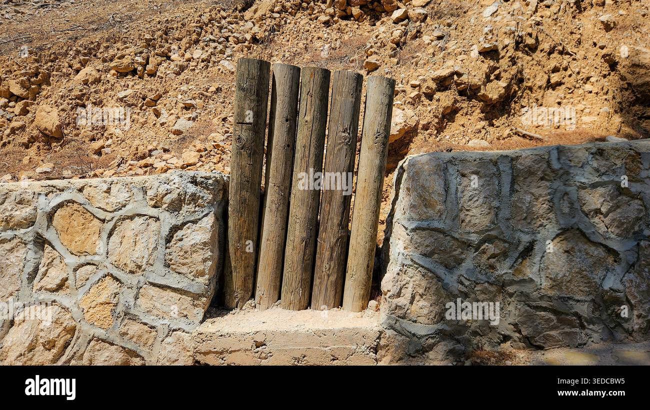 Vertikale Holzstämme, die in eine Stützmauer aus Stein eingebaut sind, veranschaulichen die Handwerkskunst der ländlichen Bausubstanz und das nachhaltige Design im Außenbereich Stockfoto