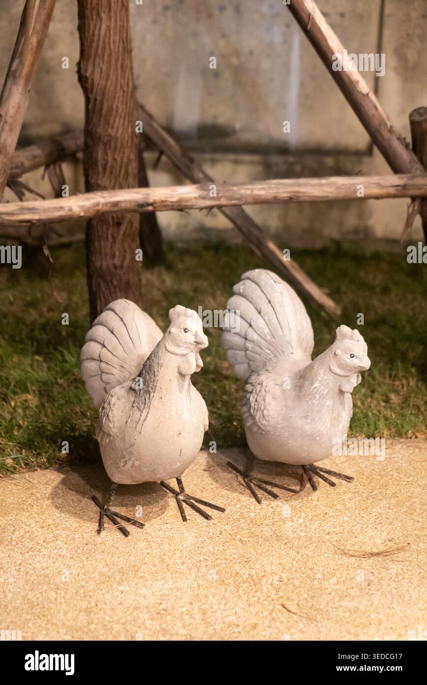 Zwei charmante Steinhühner stehen in einer rustikalen Gartenanlage und schaffen eine skurrile und friedliche Atmosphäre für jeden Außenbereich oder Dekorationsprojekt. Stockfoto