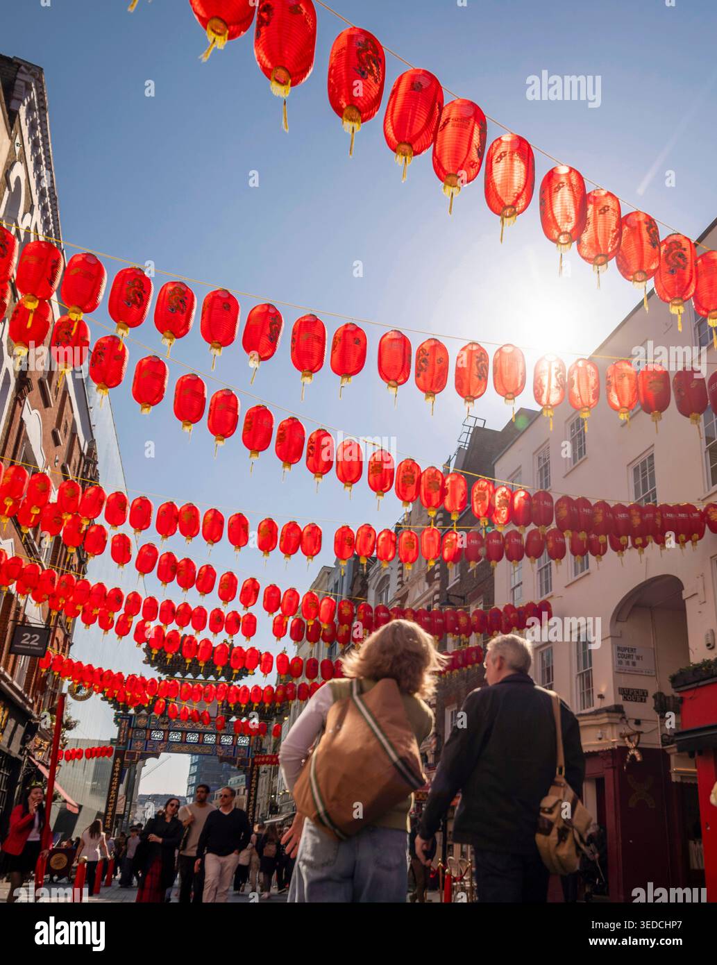 Touristen spazieren unter traditionellen roten chinesischen Laternen in Wardour Street, Chinatown, Soho, London, Großbritannien an einem sonnigen Tag Stockfoto