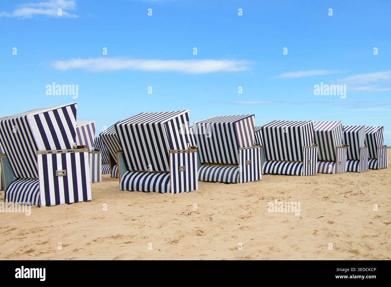 Eine Reihe traditioneller gestreifter Liegestühle aus den Windstrandkörben an einem Sandstrand an der Ostseeküste. Stockfoto