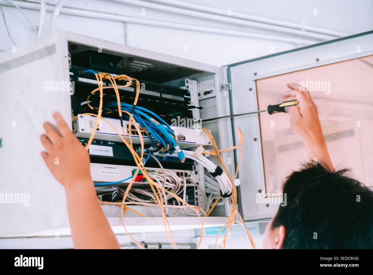 Ein Techniker führt die Netzwerkwartung innerhalb eines Serverschranks durch. Die Abbildung zeigt die komplizierten Verdrahtungen und Werkzeuge, die zur Optimierung von Verbindungen verwendet werden Stockfoto