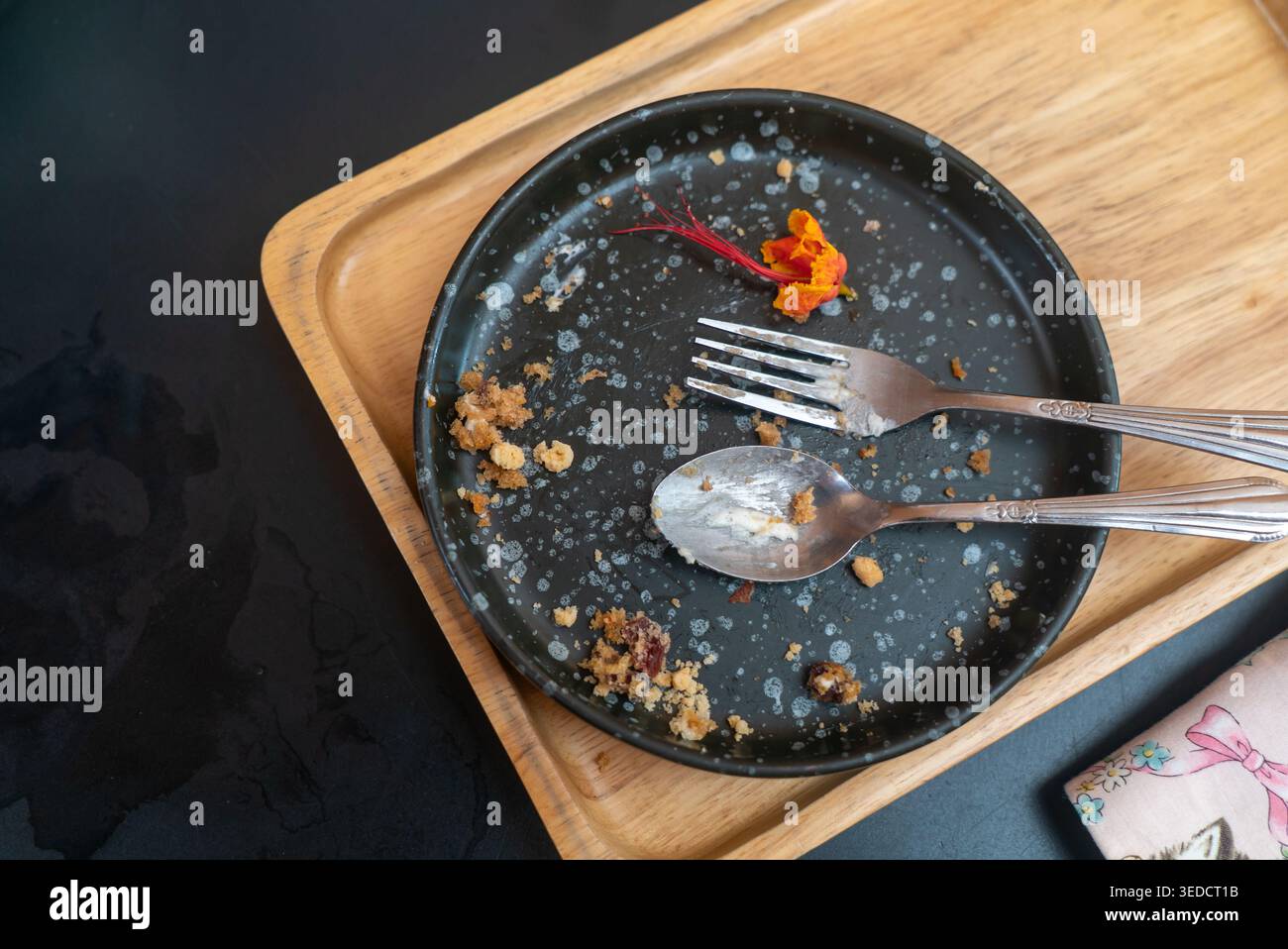 Ein leerer Teller mit Besteck mit übrig gebliebenen Krümeln und einer dekorativen Blume. Ideal für Restaurants, kulinarische Erlebnisse und Präsentationen. Stockfoto