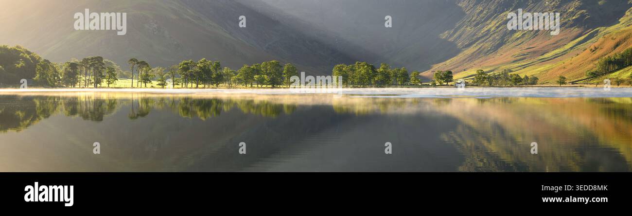Riesiger Panoramablick auf Kiefern entlang der Küste von Buttermere mit Reflexen im See. Stockfoto