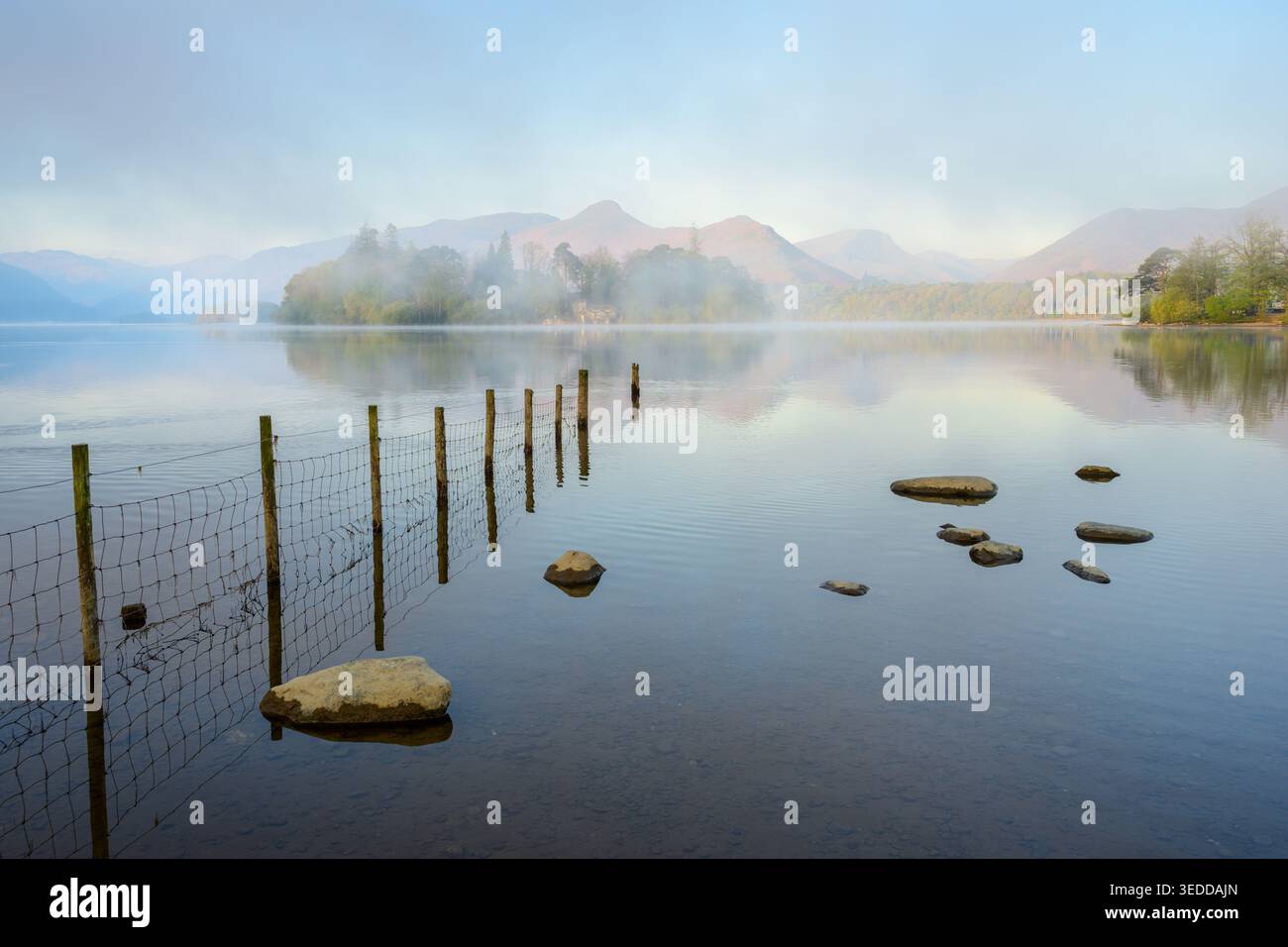 Malerischer Blick auf Derwentwater an einem nebeligen Frühlingsmorgen mit Zaun und Felsen im Wasser. Crow Park, Lake District, Großbritannien. Stockfoto
