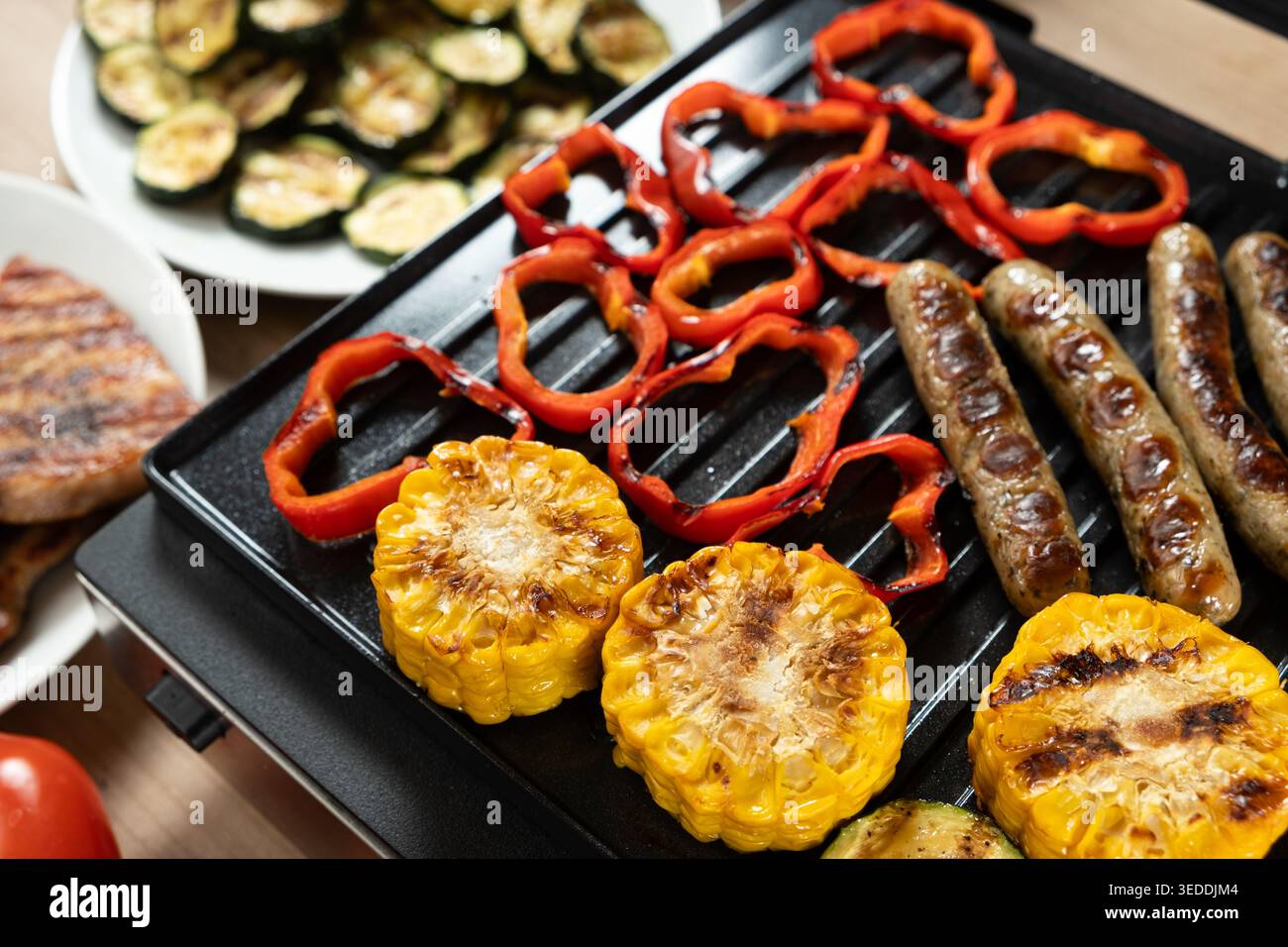 Gegrillte Würstchen mit Mais, Paprika und Zucchini auf heißem Grill. Stockfoto