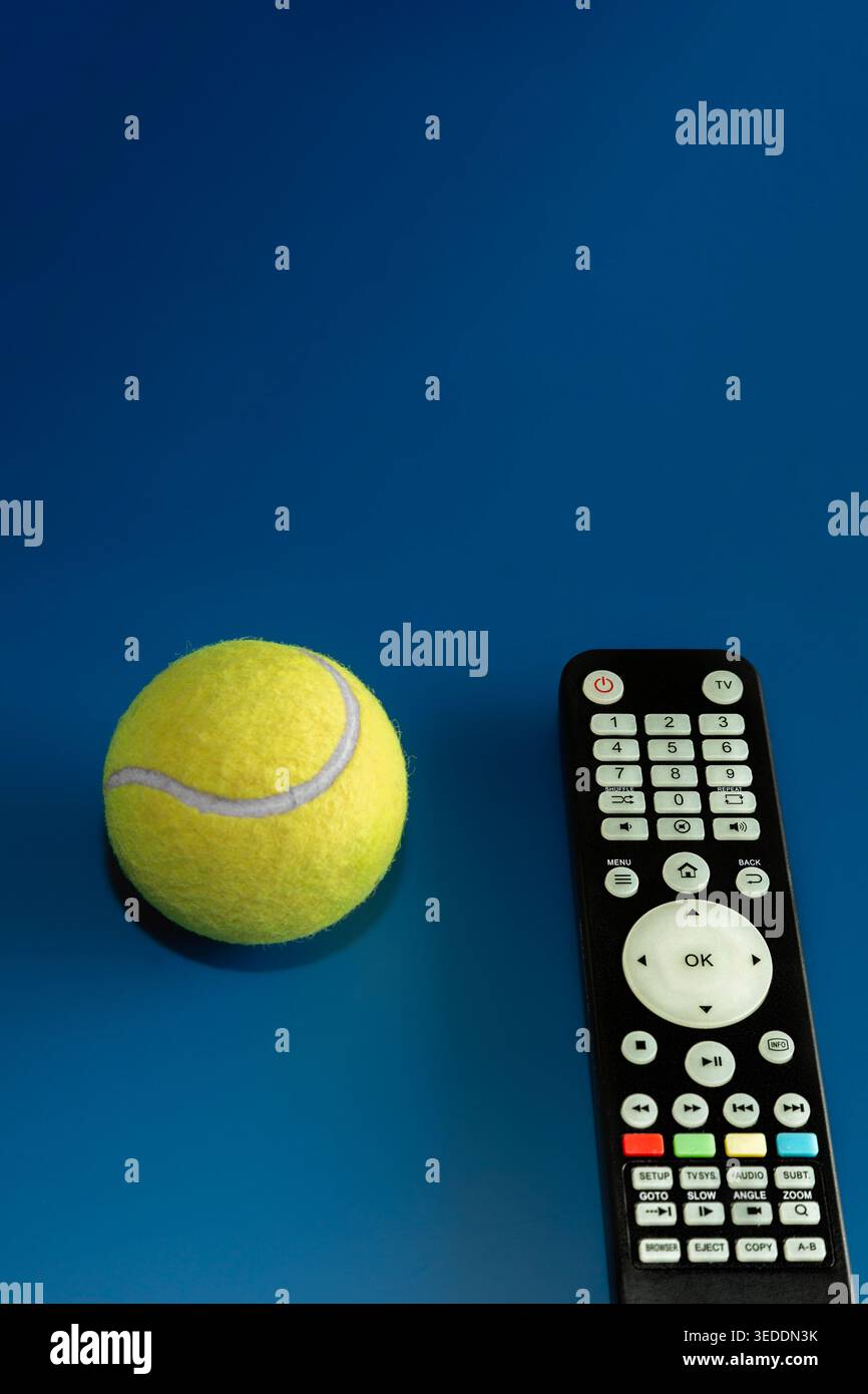 Gelber Tennisball mit schwarzer Fernbedienung auf blauem Hintergrund für Sport-Streaming-Konzept. Stockfoto