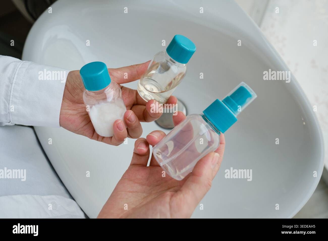 Person in einem weißen Hemd, die zwei kleine durchsichtige Plastikflaschen mit blauen Kappen auf den Handflächen hält Stockfoto