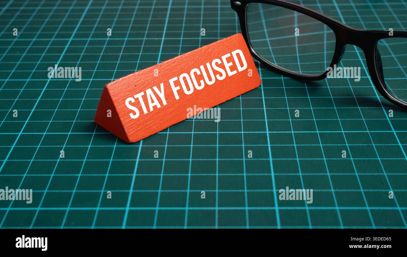 Bleiben Sie fokussiert Text auf rotem Dreiecksblock mit Brille auf grünem Gitterhintergrund für ein Produktivitätskonzept Stockfoto