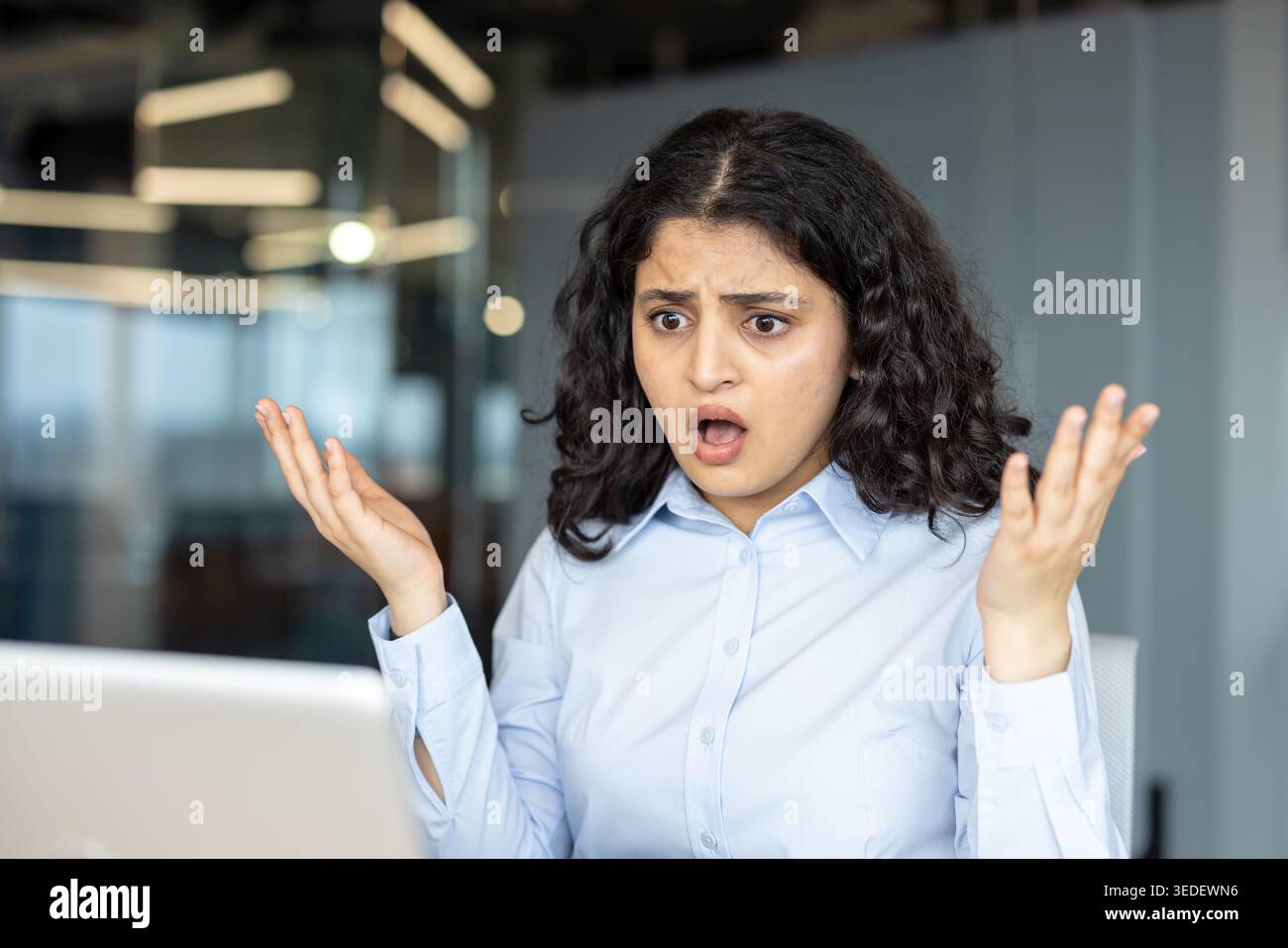 Indische Profi-Frau an ihrem Laptop reagiert mit Schock und Frustration auf einen plötzlichen Systemfehler, während sie ferngesteuert oder in einem modernen Büro arbeitet, von Hand zu Gesicht, besorgt ausdrucksstark Stockfoto