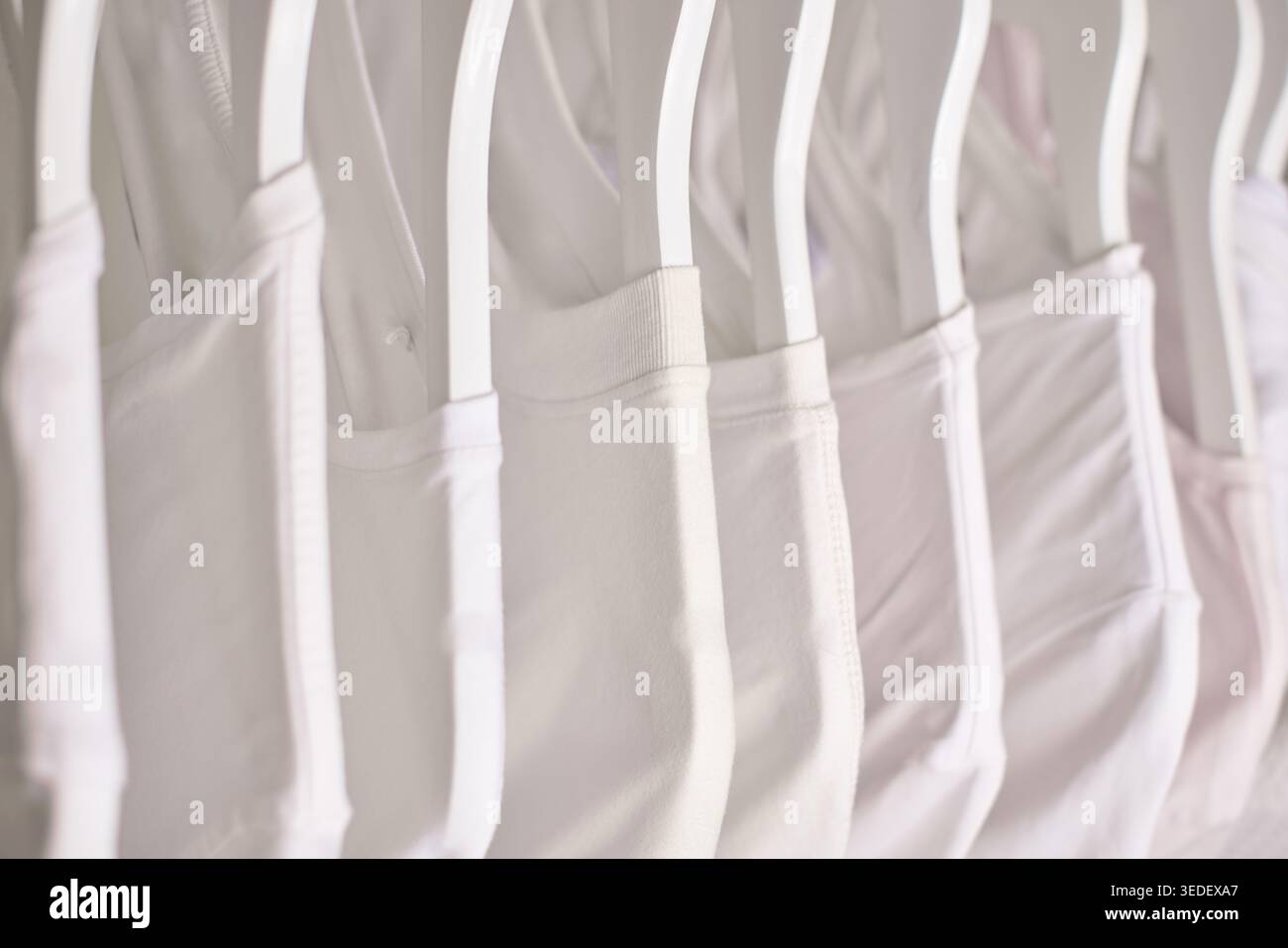 Weiße und helle Hemden zeigen Minimalismus, Organisation und Sauberkeit und hängen ordentlich auf einem Kleiderständer Stockfoto