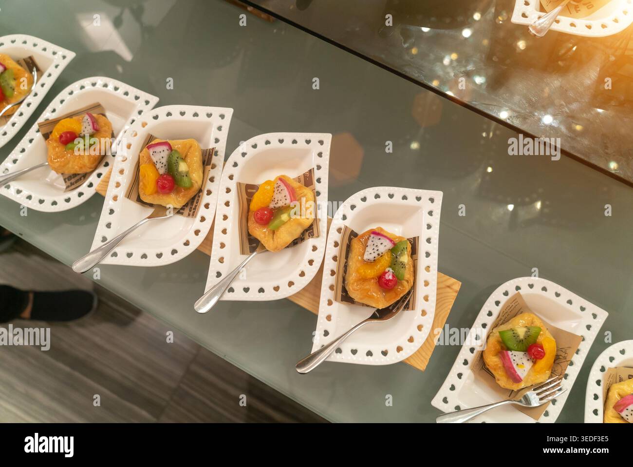 Ein wunderbares Arrangement von farbenfrohen Obstkuchen auf dekorativen Tellern, perfekt für Veranstaltungen, Partys oder Catering-Services, mit frischem i Stockfoto