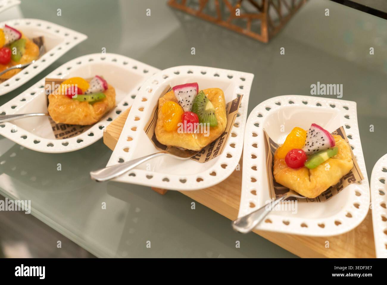 Farbenfrohe Obsttörtchen sind wunderschön auf eleganten Desserttellern angeordnet. Jede Tarte bietet eine Kombination aus frischen Früchten, die Farbe und Geschmack verleihen. Stockfoto
