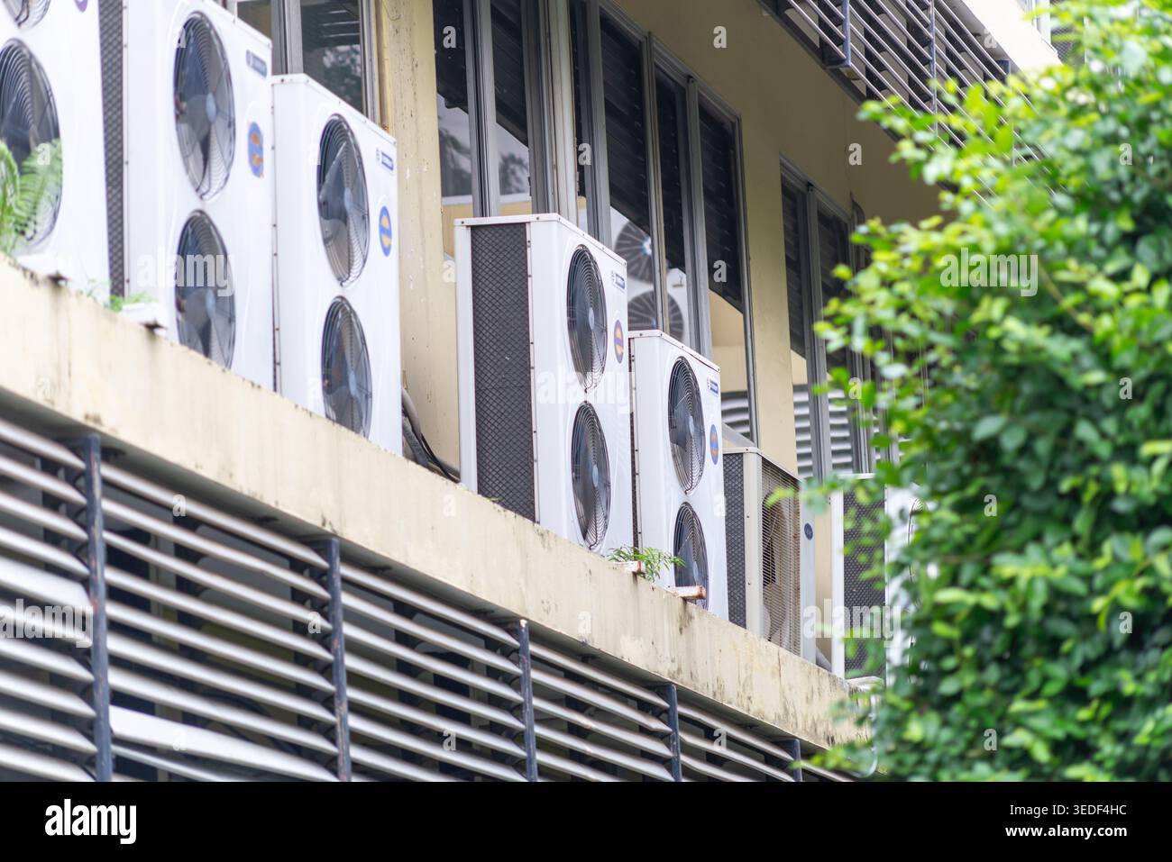 Eine Reihe von Klimaanlagen, die an der Außenseite eines Gebäudes montiert sind und die von Grün umgebene städtische Klimaregelungstechnik demonstrieren. Stockfoto