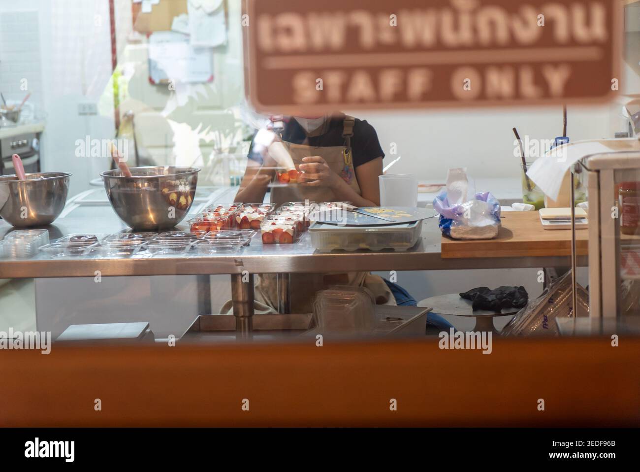 Werfen Sie einen Blick in eine Bäckereiküche, in der die Mitarbeiter verschiedene Desserts zubereiten und eine kreative Kochumgebung voller Zutaten und Werkzeuge präsentieren. Stockfoto