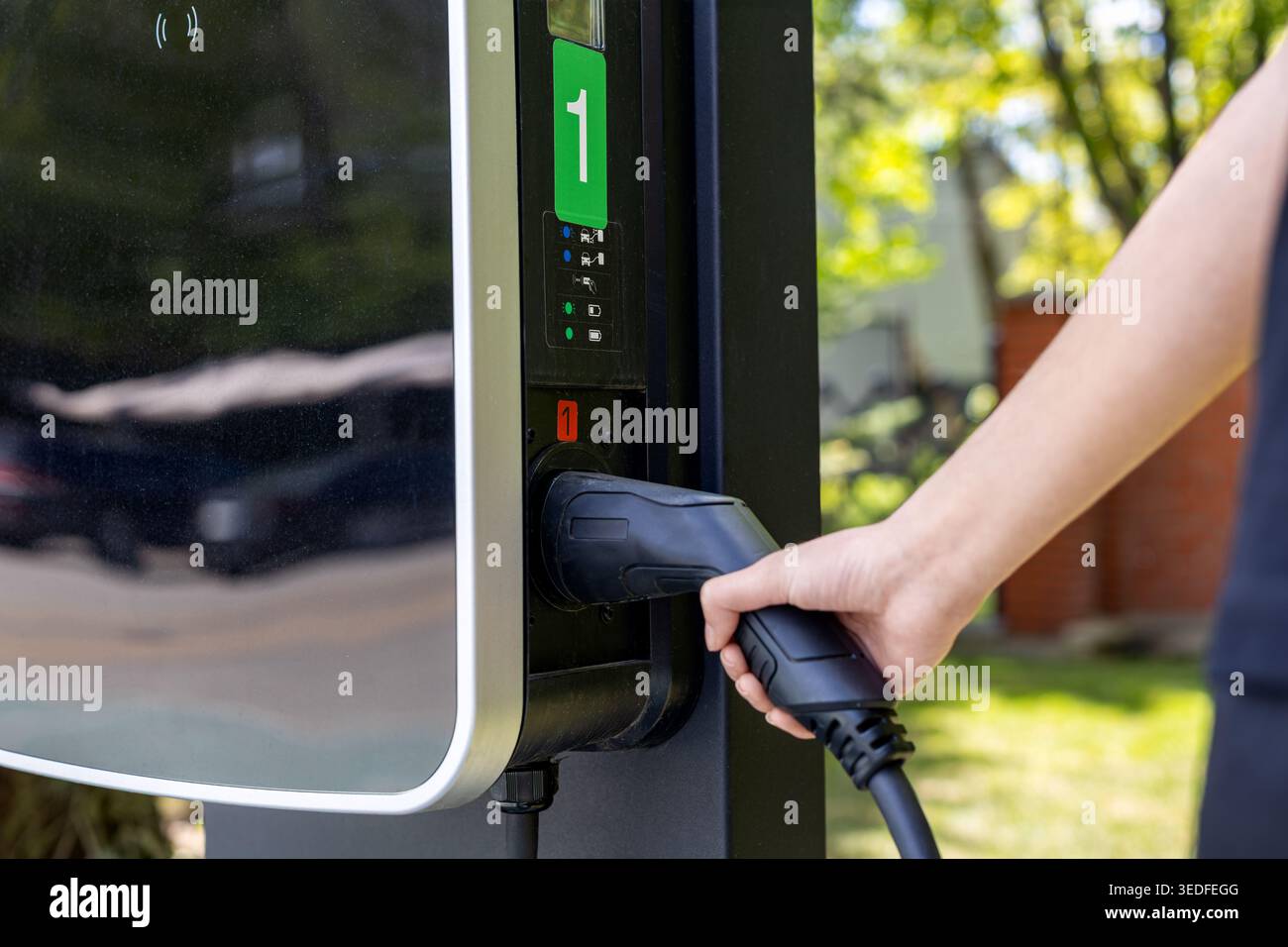 Stecken Sie das Kabel von Hand in das EV-Ladegerät. Nahaufnahme einer Hand, die ein Elektrofahrzeug-Ladekabel mit einer öffentlichen Außenladestation verbindet. Stockfoto