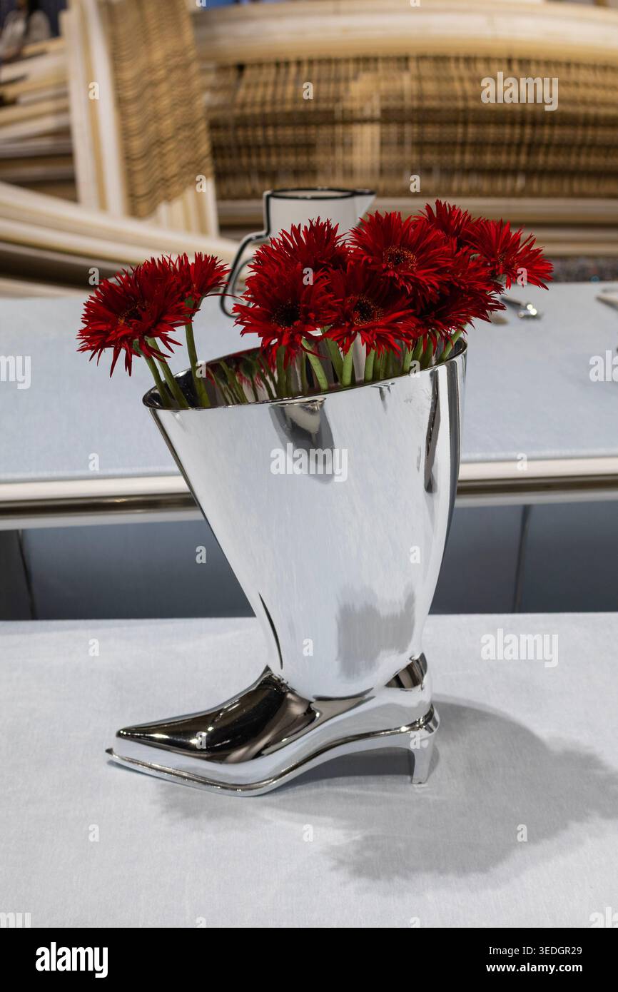 Rote Blumen in einer modernen Metallic-Vase, geformt wie ein High-Heel-Schuh. Stilvolles Blumendesign und modernes Innendekor-Konzept. Stockfoto