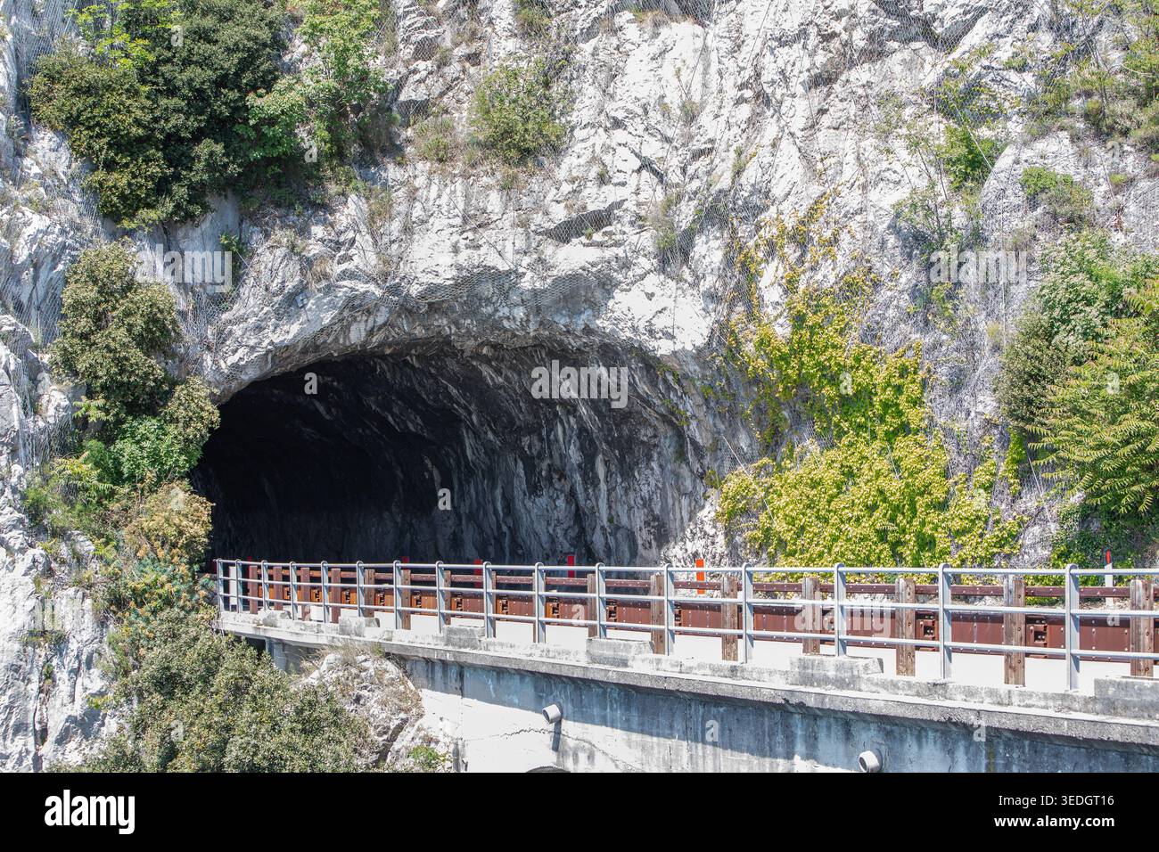 Bergstraße, die in einen dunklen Felstunnel mit Betonbarriere führt Stockfoto