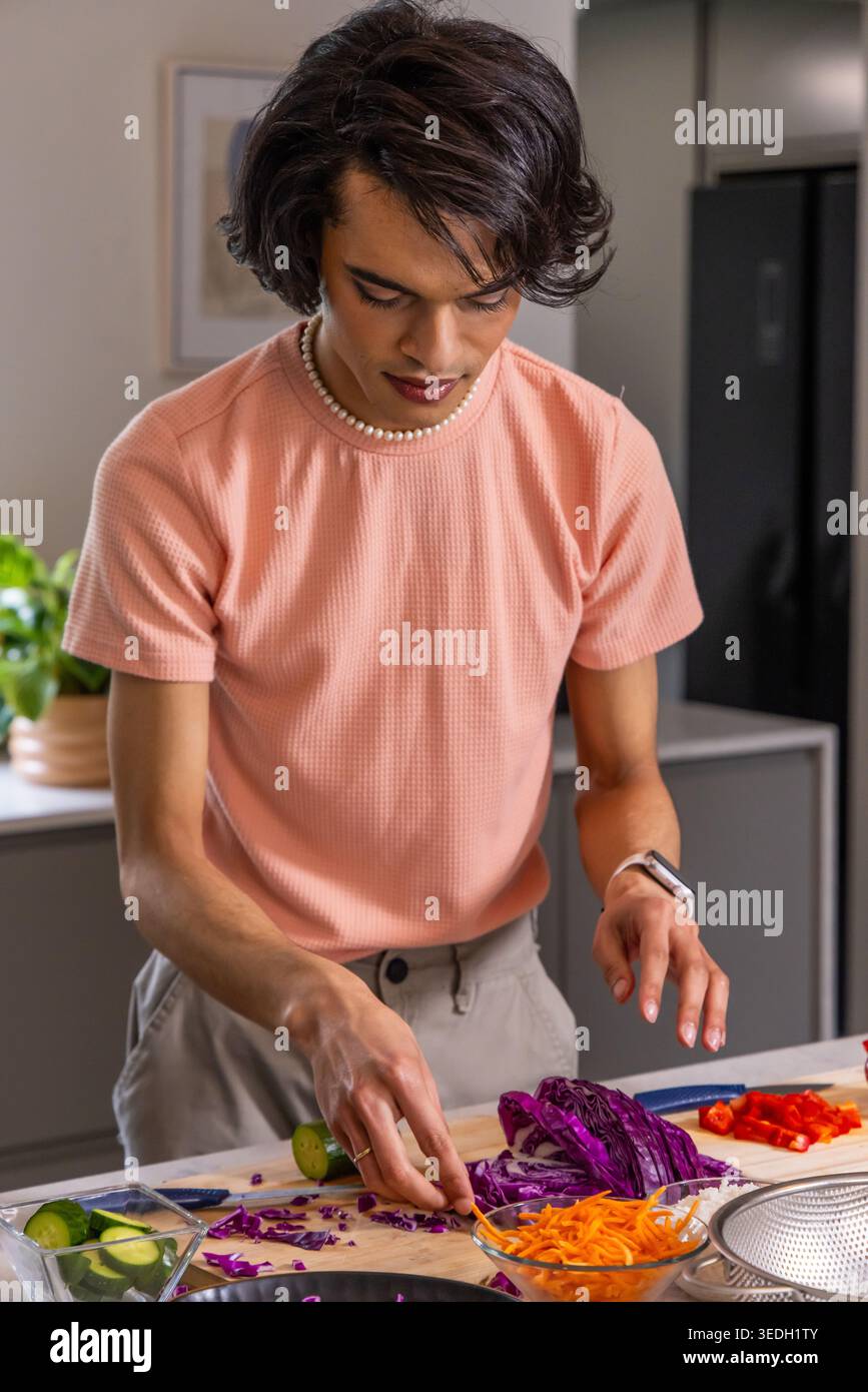 Mann in 20ern, der Purpurkohl mit Kochmesser auf Schneidebrett in der Küche hackt, Pfirsichhemd Stockfoto