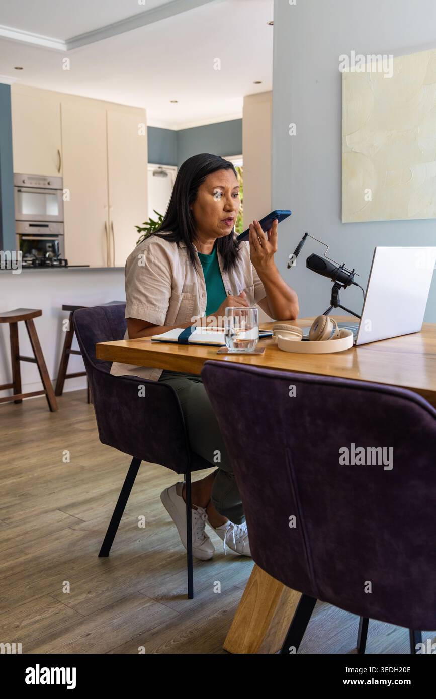 Asiatische Frau, die das Smartphone am Mund hält und zu Hause mit Laptop und Mikrofon aufnimmt Stockfoto