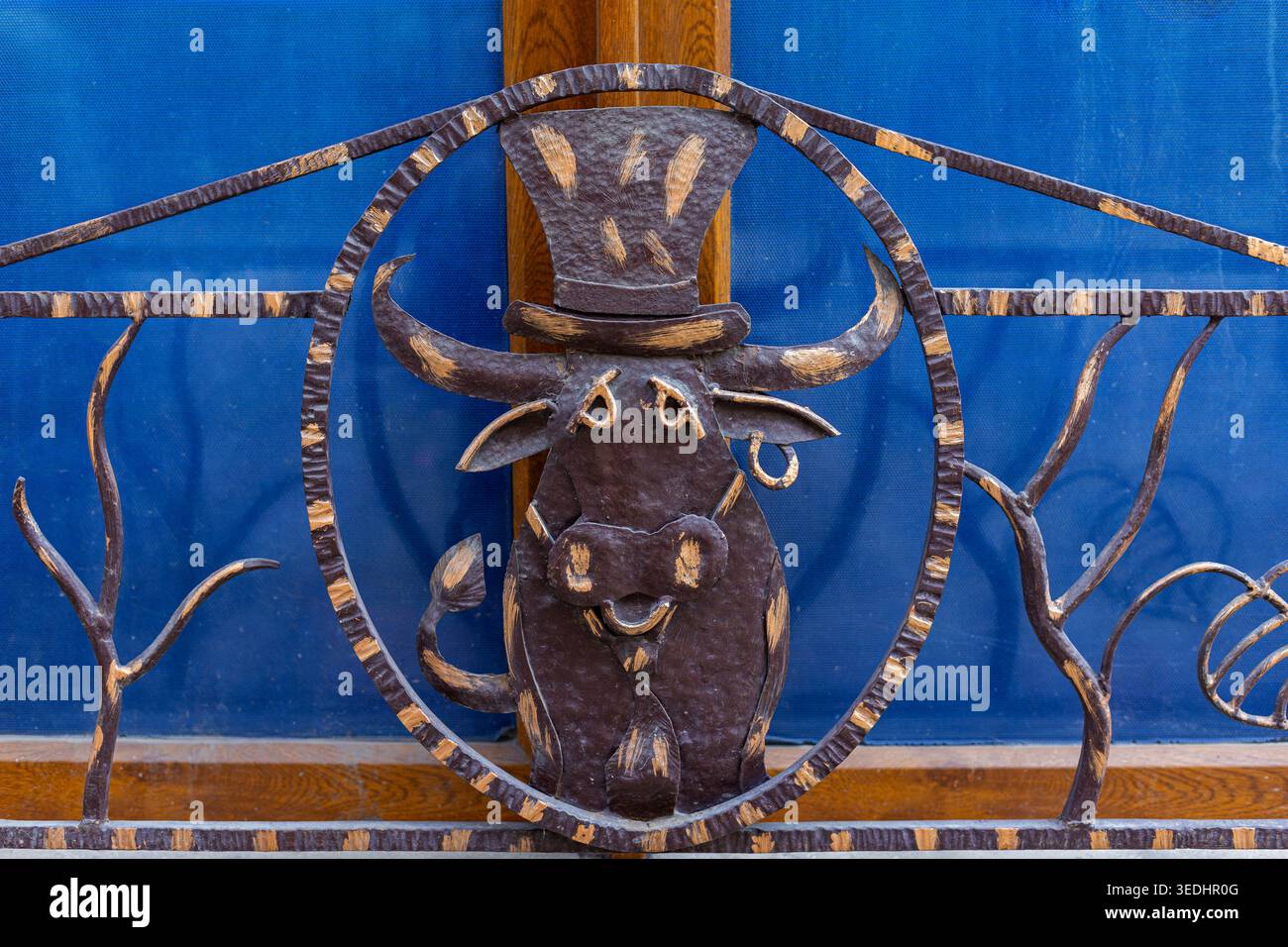 Dekoratives Metall-Bull-Gate-Ornament. Nahaufnahme eines rustikalen schmiedeeisernen Bullen mit Hut, der als dekorative Metallarbeiten an einem Tor oder Geländer verwendet wird. Stockfoto