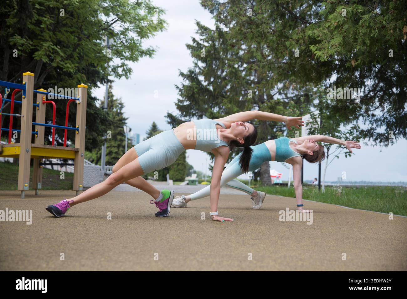 Sportliche zwei Frauen im Sportoutfit, die morgens trainieren und sich auf dem Straßensportplatz Strecken. Fitness-Workout auf dem Sportplatz. Ausbildung bei einem Inruktor in der Natur Stockfoto