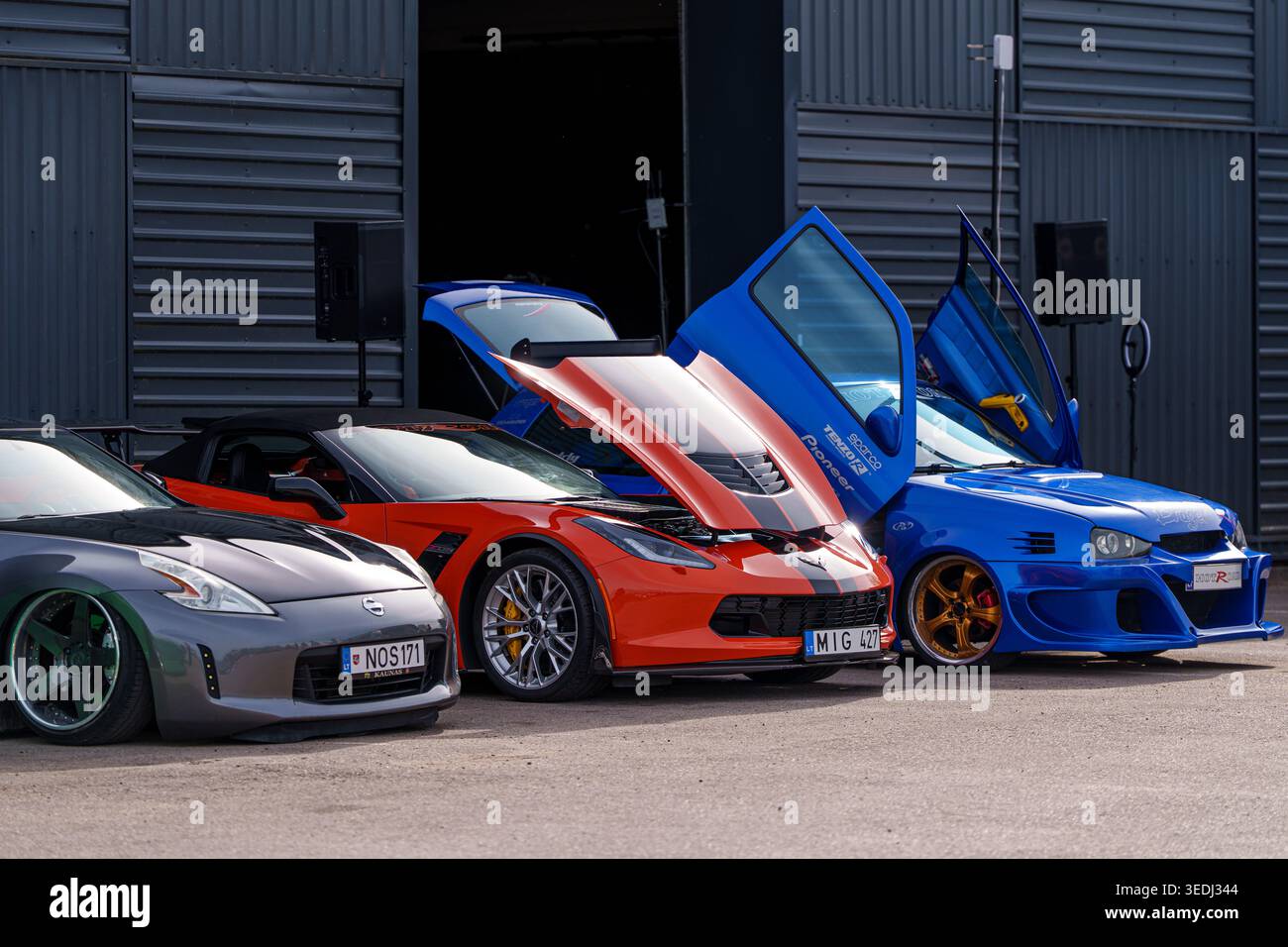 Gruppe modifizierter Performance-Fahrzeuge, darunter ein grauer Nissan 370Z, ein orangefarbener Chevrolet Corvette und ein blauer Volkswagen Golf mit vertikalen Scherentüren an A Stockfoto