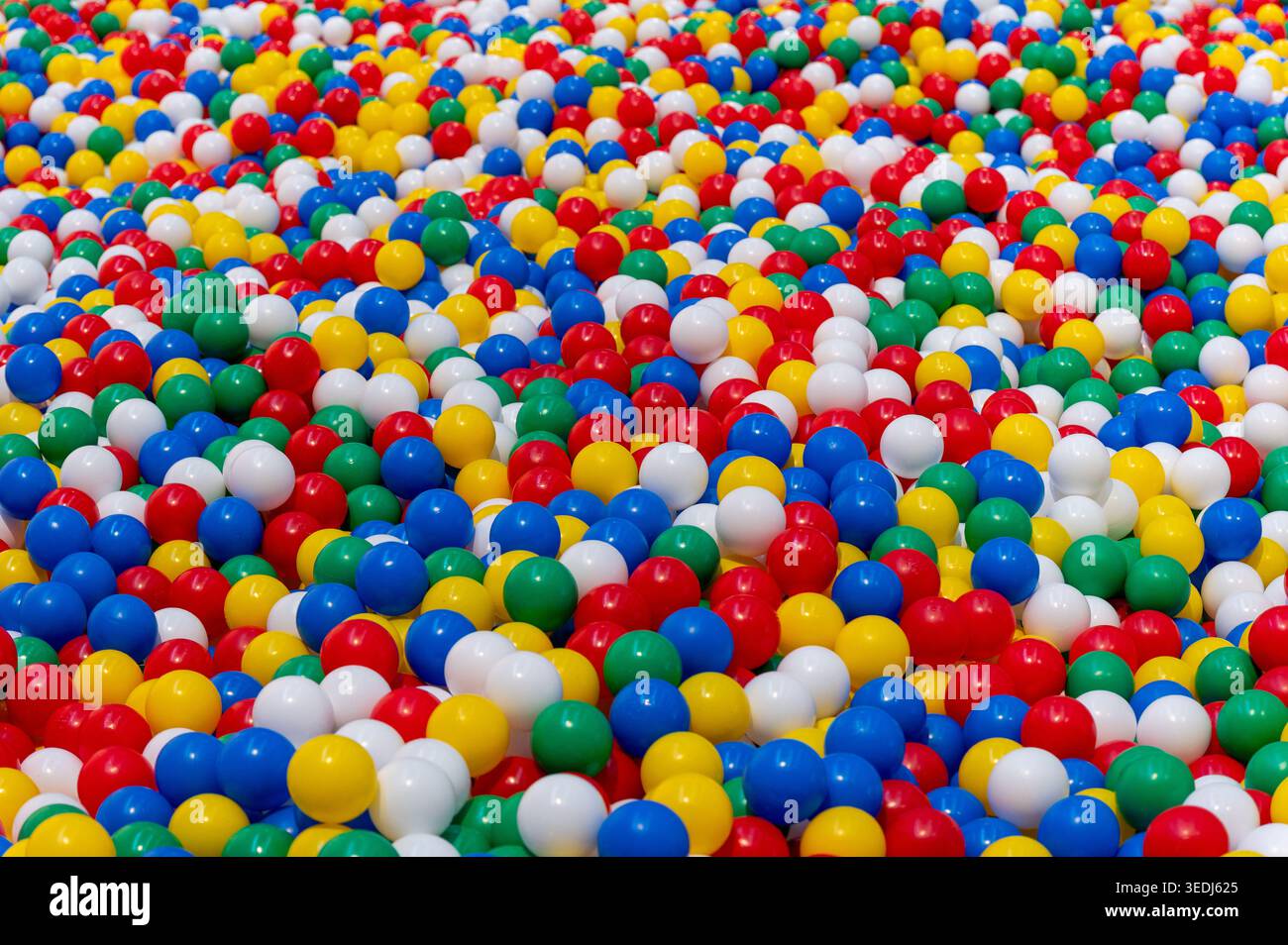 Tausende von leuchtenden roten, blauen, grünen, gelben und weißen Plastikkugeln schaffen einen fröhlichen Hintergrund Stockfoto