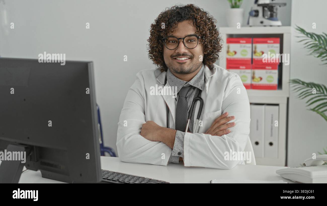 Mann Doktor mit Stethoskop, Arme überkreuzt am Klinikpult, lächelt in die Kamera, Mitgefühl Selbstvertrauen. Stockfoto