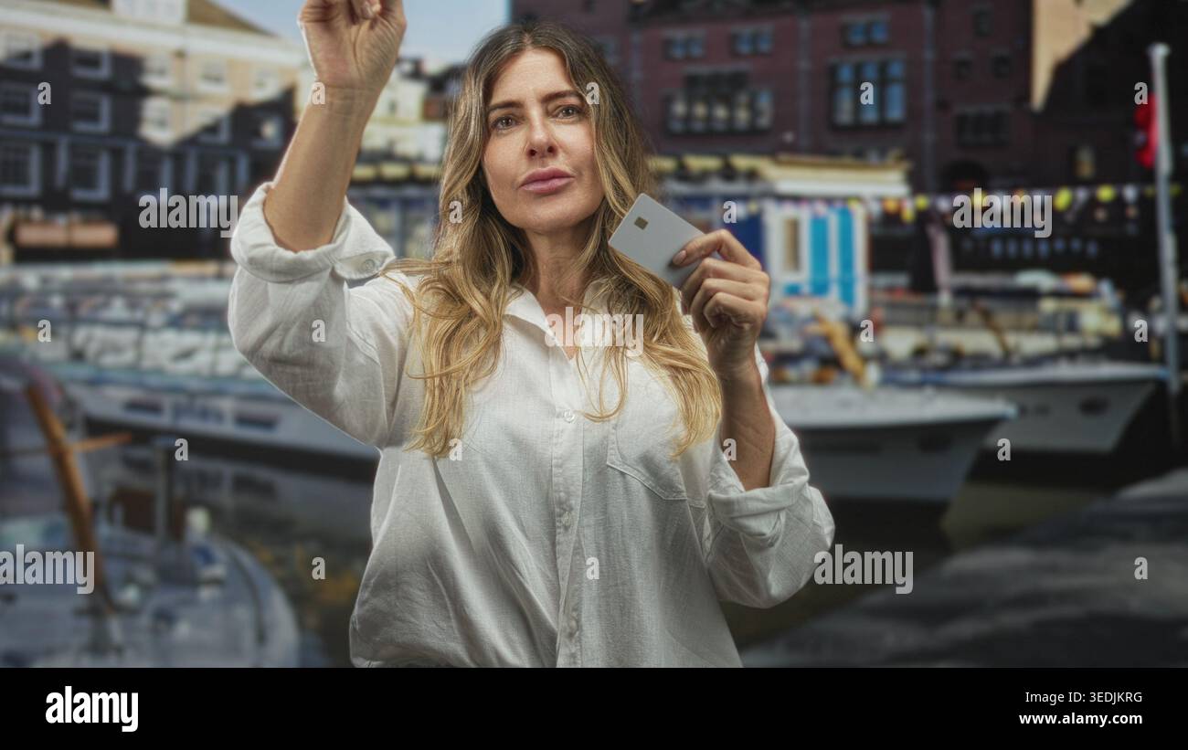 Frau, die eine Kreditkarte hält und mit dem Finger nach vorne zeigt, mit Booten am Hafen; Selbstvertrauen stärken. Stockfoto