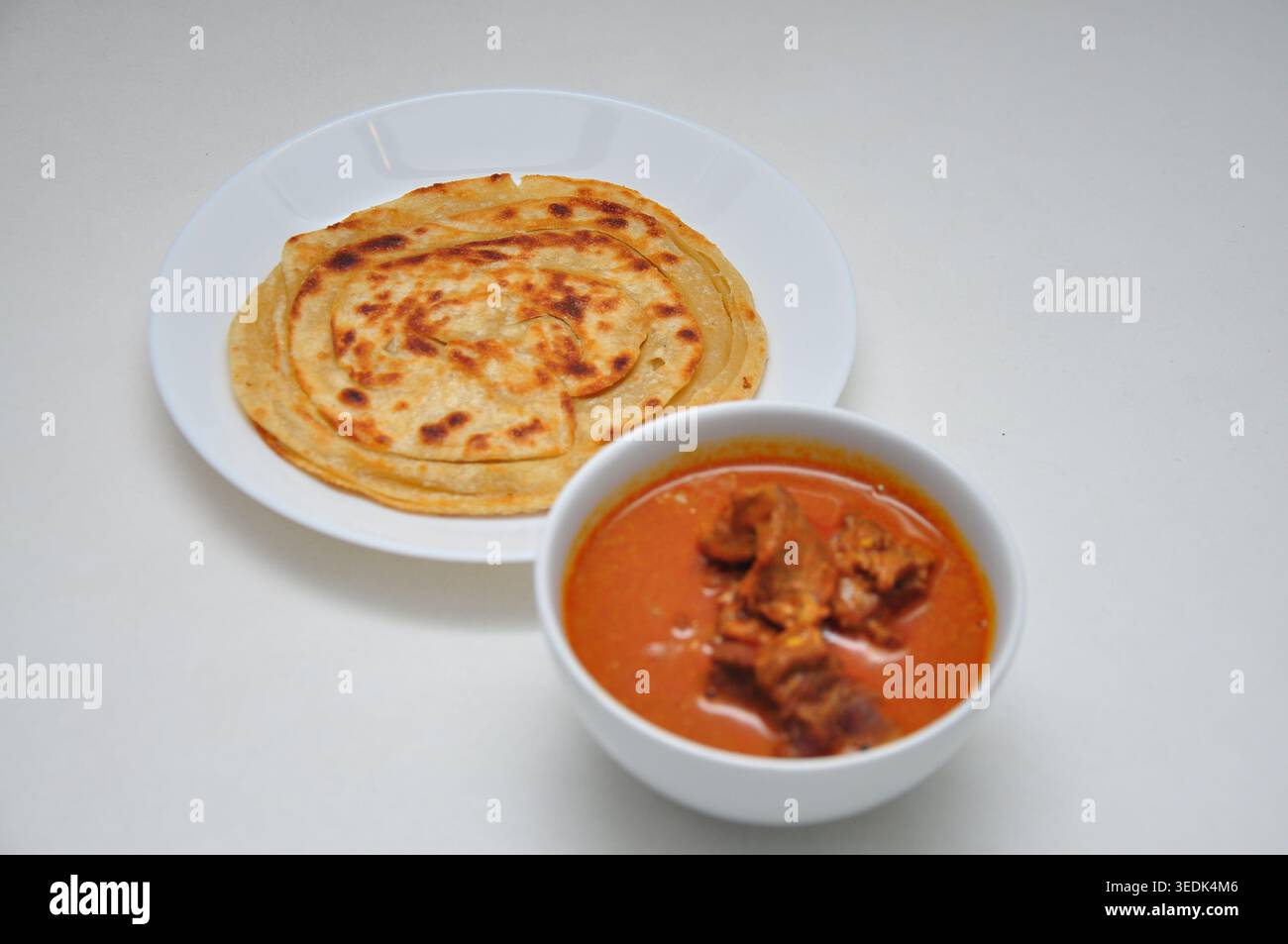 Herzhafte Roti Paratha oder Pratha nach indischer Art, serviert mit Hammel- oder Lammcurry auf weißem Teller auf weißem Tisch Stockfoto