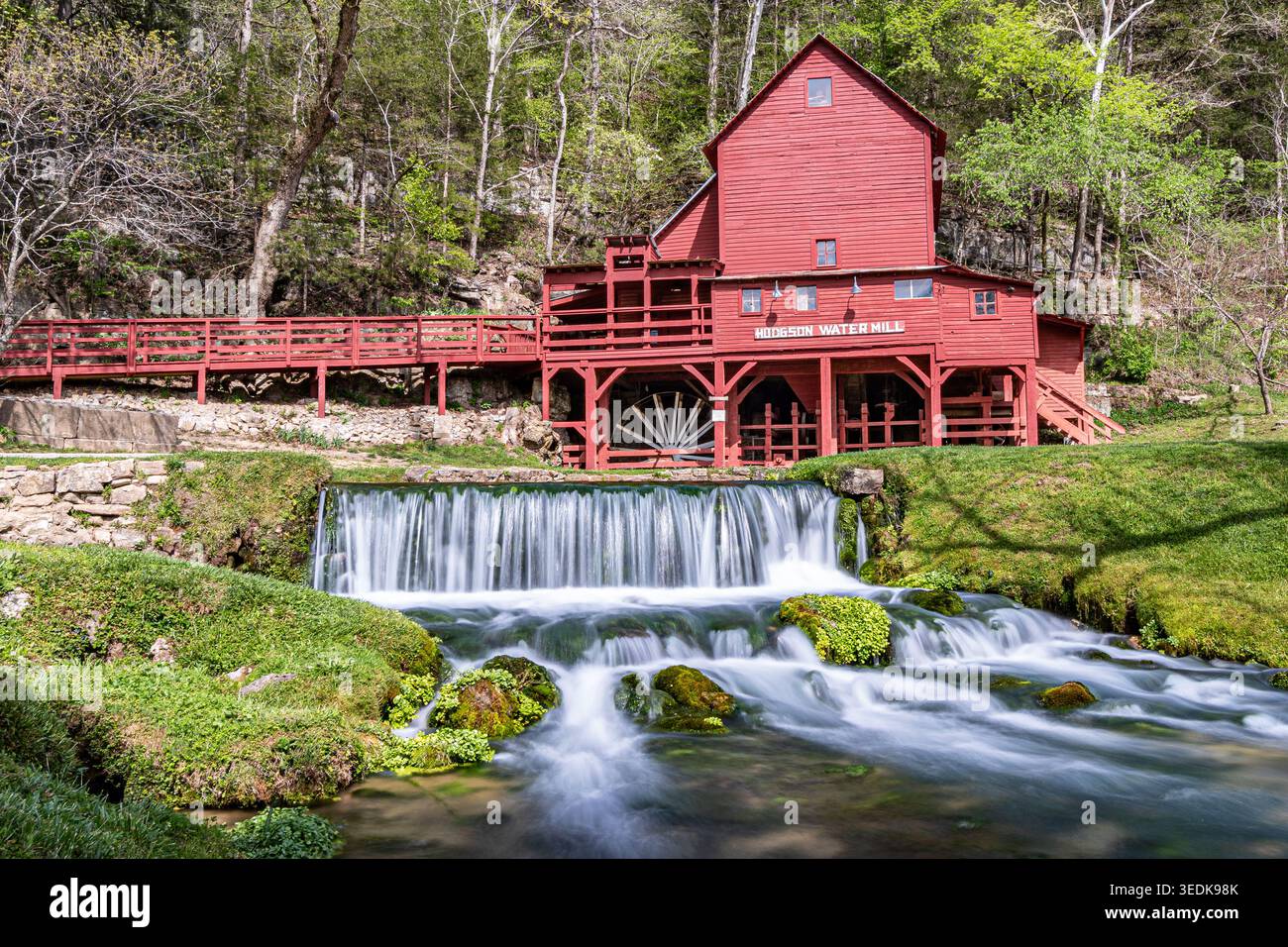 Dieses lebhafte Foto zeigt die berühmte Hodgson Water Mill (1897), deren scheunrote Seite einen auffälligen Kontrast zum üppigen Frühlingslaub in Ozark bildet. Stockfoto