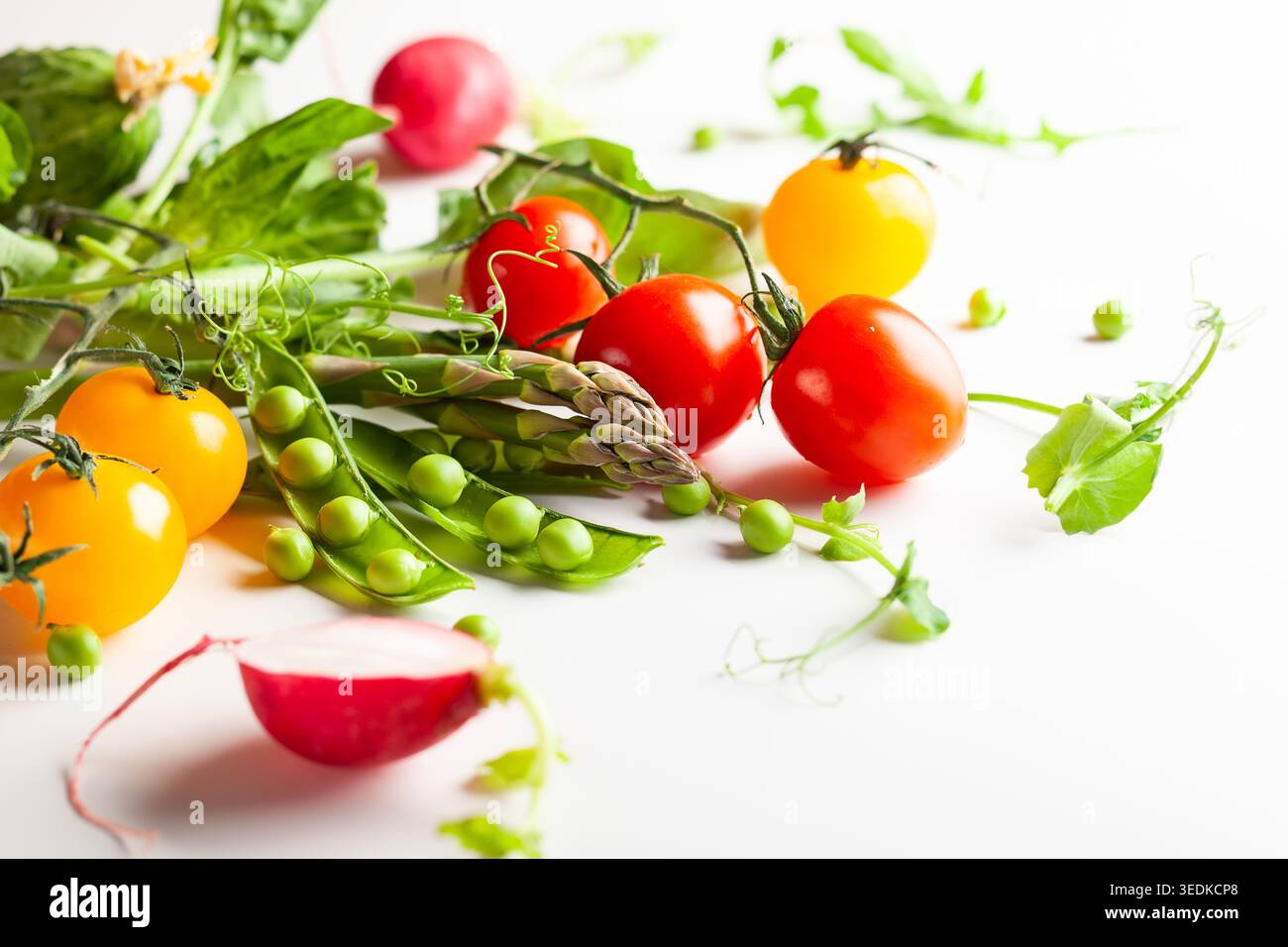 Frische grüne Erbsenschoten mit Sprossen, Rettich, Tomaten und grünem Spargel auf weißem hölzernem Hintergrund. Konzept der gesunden Ernährung, frisches Gemüse. Stockfoto