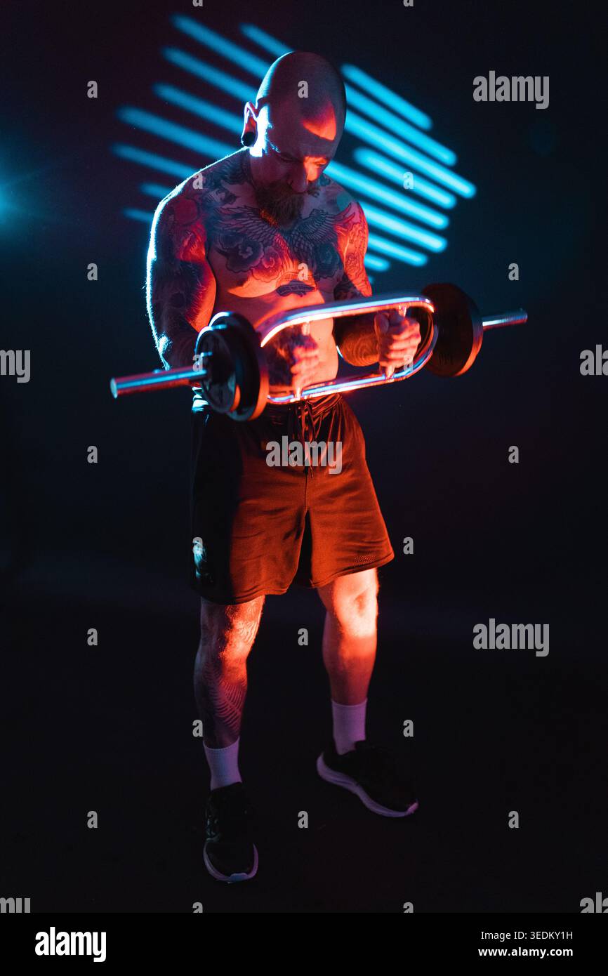 Mann hebt während eines Workouts eine Langhantel in einem dunklen Raum mit farbigen Lichtern in einem Fitnessstudio Stockfoto