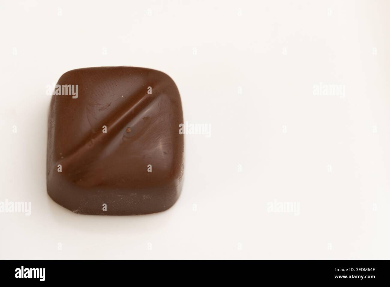 Minimalistische quadratische Milchschokolade-Praline mit diagonalem Detail auf weißem Hintergrund Stockfoto