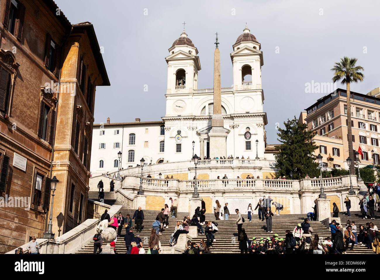 Menschen sitzen auf der Spanischen Treppe auf der Piazza di Spagna mit der Renaissance-Kirche Trinità dei Monti auf der Spitze in Rom, Italien. Stockfoto