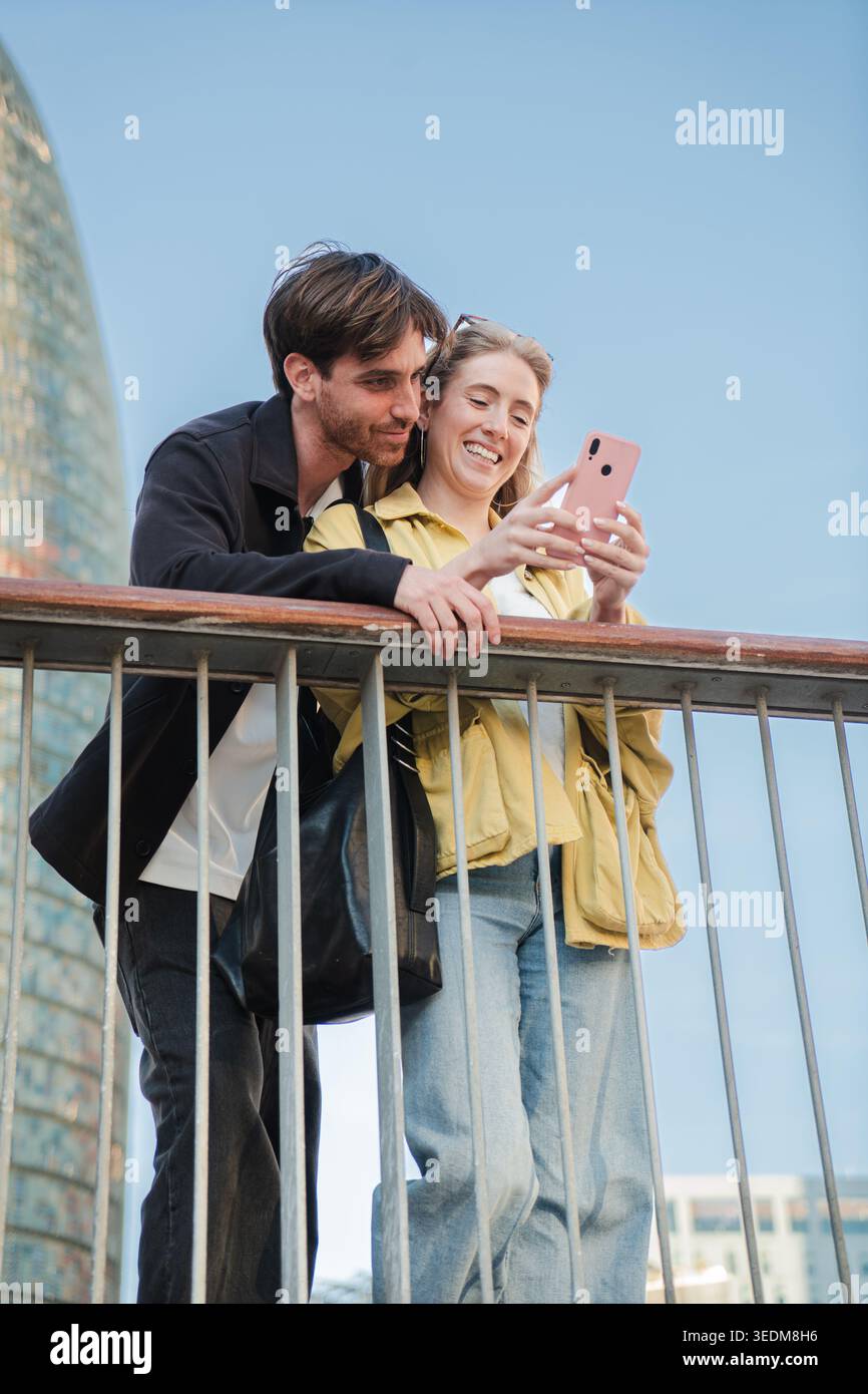 Glückliches Paar, das zusammen ein entzückendes Selfie einfängt, sich vor Freude und Lachen über ein Geländer beugt und ihre Zuneigung und Begeisterung für zeigt Stockfoto