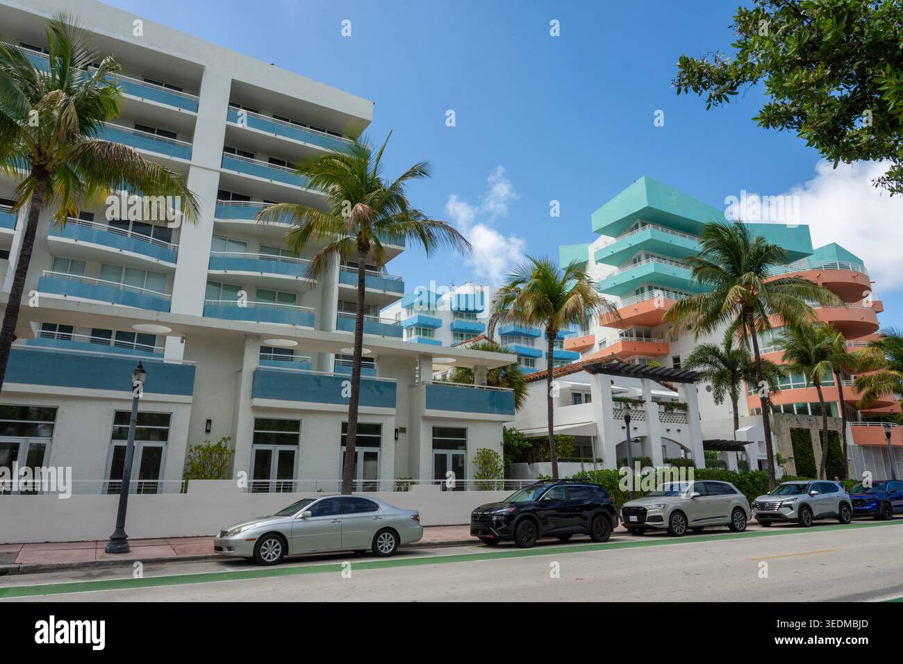 Farbenfrohe moderne Apartmentgebäude im Art déco-Stil und Luxusautos, die unter Palmen in Miami Beach, Florida, geparkt werden. Eine lebendige urbane Szene. Stockfoto