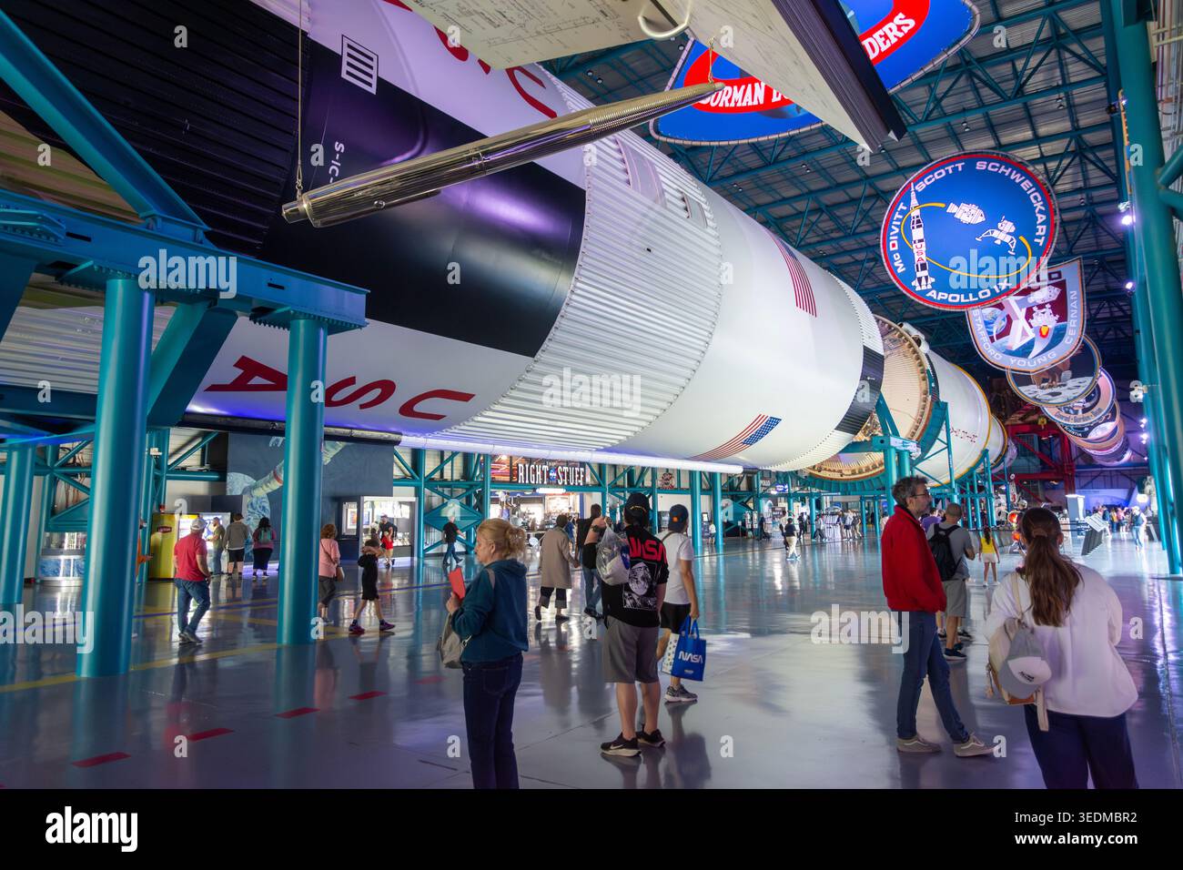 Touristen spazieren unter der riesigen Saturn-V-Rakete im Apollo/Saturn V Center im Kennedy Space Center. Ein beeindruckender Skalenvergleich. Stockfoto
