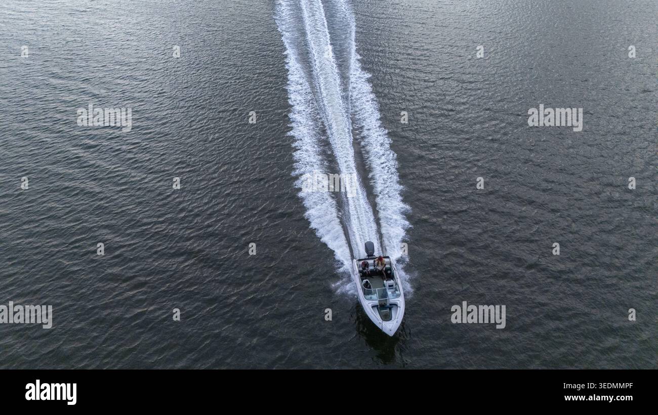 Aus der Vogelperspektive eines Motorbootes, das durch dunkles Wasser fährt, mit Menschen an Bord und einem langen weißen Wake hinter Badagry, Lagos, Nigeria. Stockfoto