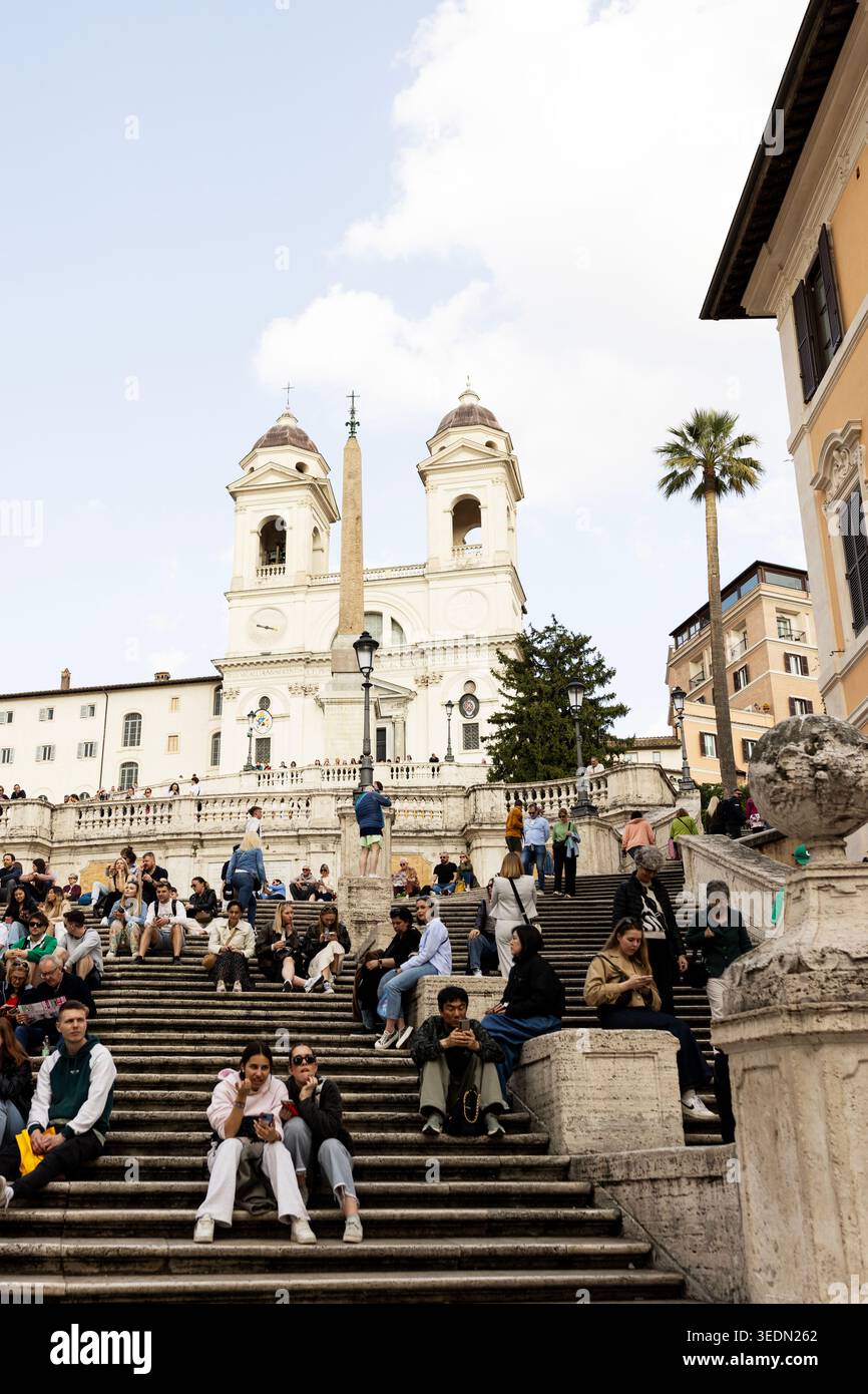 Menschen sitzen auf der Spanischen Treppe auf der Piazza di Spagna mit der Renaissance-Kirche Trinità dei Monti auf der Spitze in Rom, Italien. Stockfoto