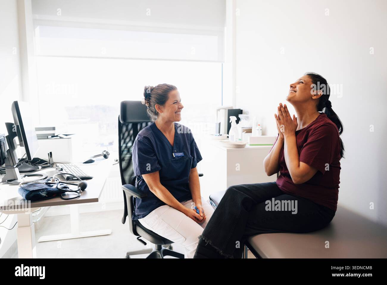 Glückliche weibliche Gesundheitsfachkraft, die in der Nähe der Frau sitzt und Dankbarkeit zeigt, nachdem sie gute Nachrichten im Krankenhaus gehört hat Stockfoto