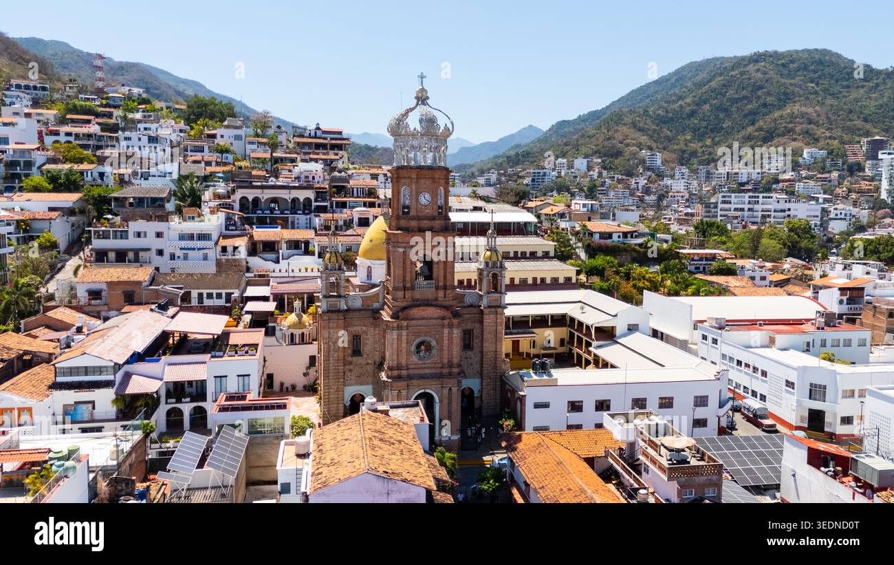 Blick aus der vogelperspektive auf die Pfarrei unserer Lieben Frau von Guadalupe mit ihrem berühmten Kronturm, umgeben von Terrakotta-Dächern und üppigen grünen Hügeln unter einem klaren bl Stockfoto