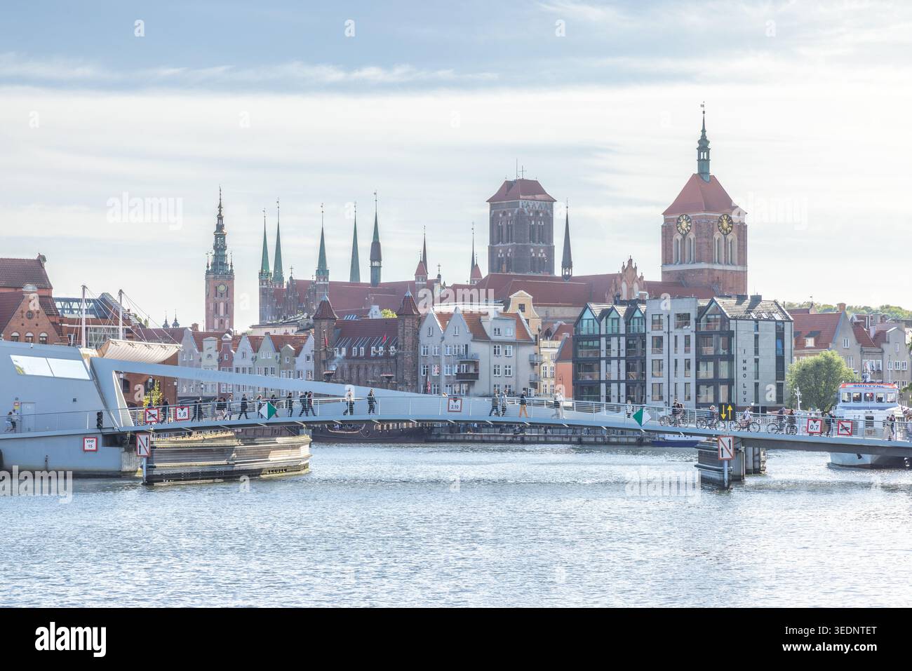Danzig, Polen - 3. Mai 2025: Blick auf die Stadt mit einer modernen Fußgängerbrücke über den Fluss Motlawa mit historischen Gebäuden im Hintergrund. Stockfoto