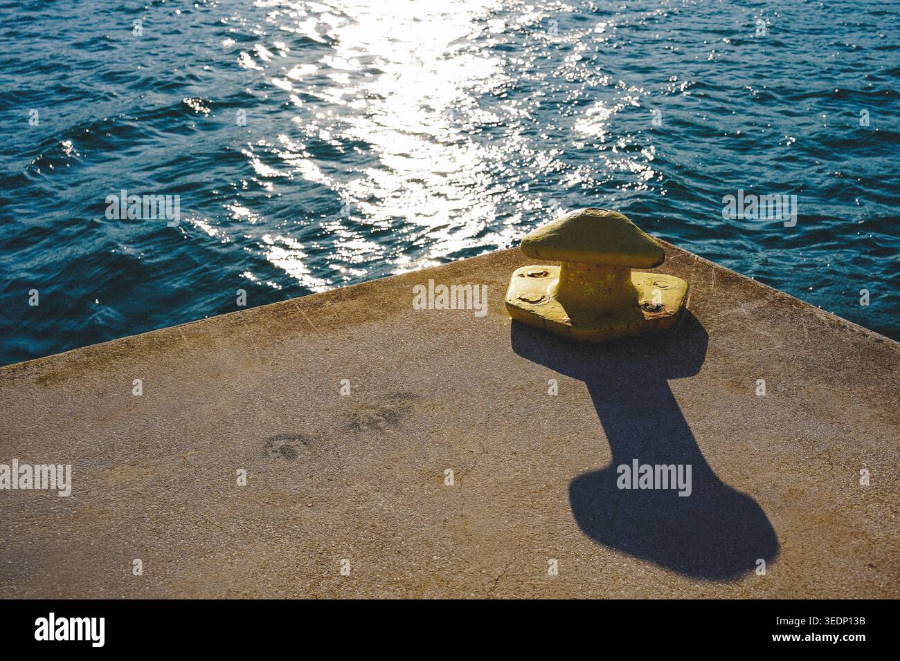 Gelber Schiffspoller mit langem Schatten am sonnendurchfluteten Hafenpier Stockfoto