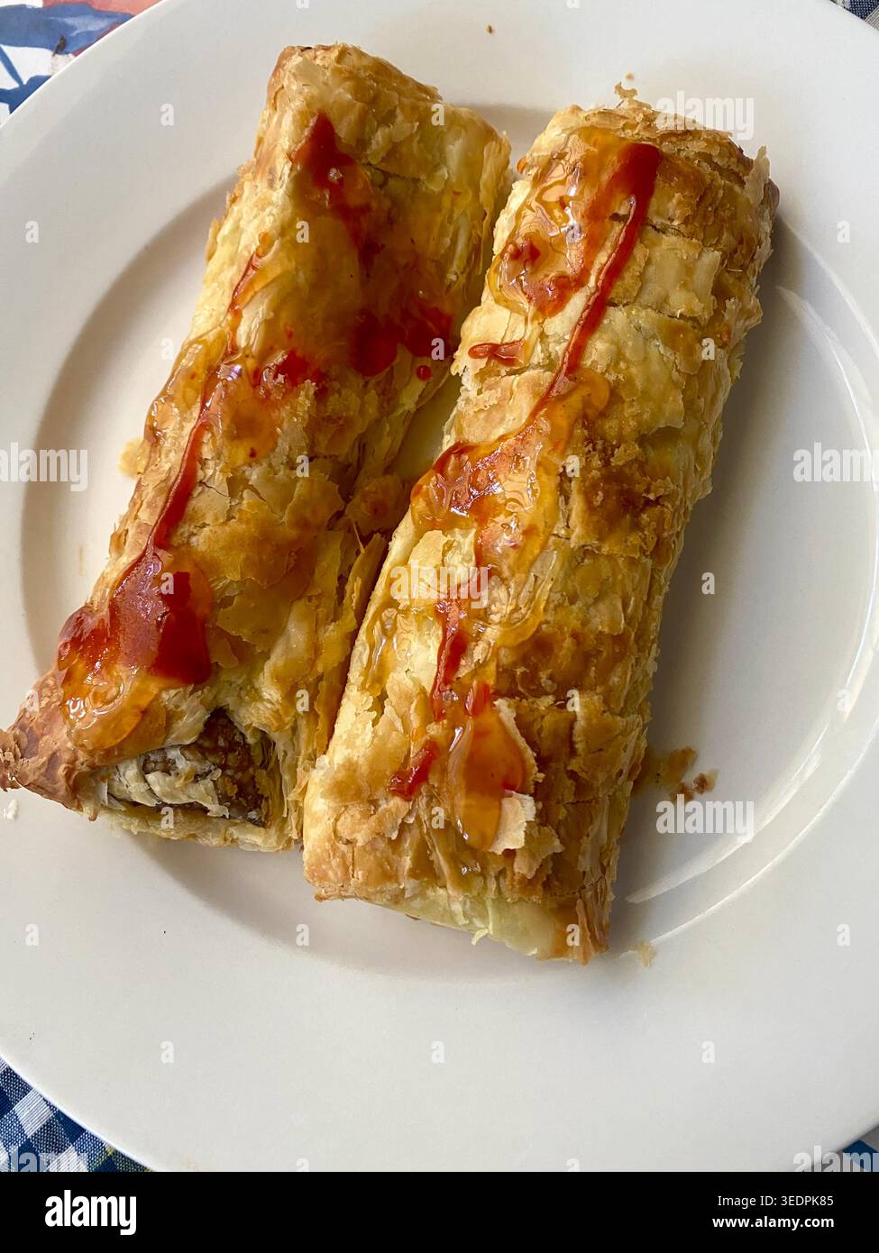 Zwei Wurstbrötchen mit Chili- und Sriracha-Sauce auf einem weißen Teller als Snack Stockfoto