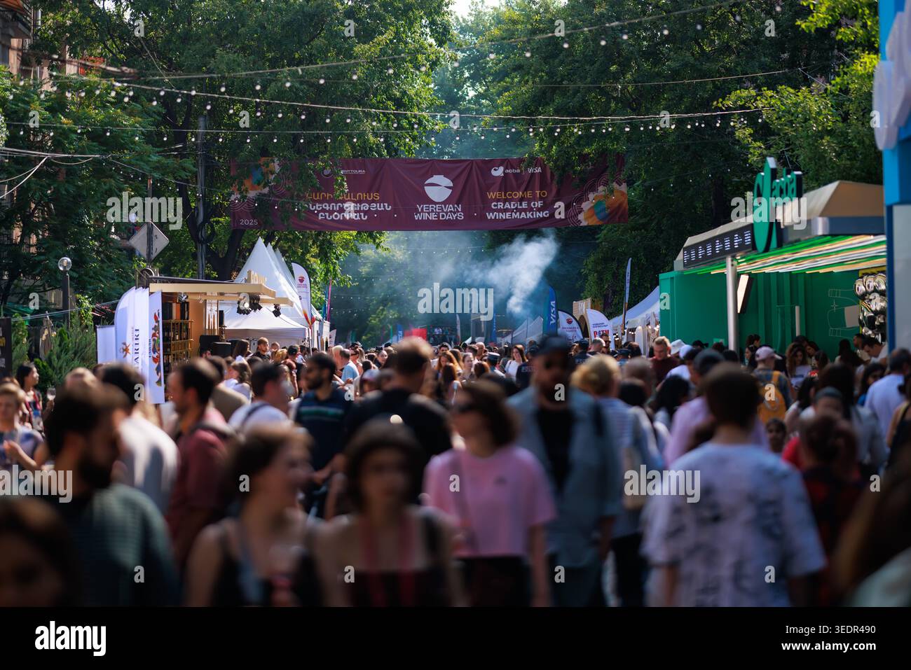 Beim Yerevan Wine Days Festival spazieren die Besucher während des Festivals entlang einer überfüllten Festivalstraße, gesäumt von Verkostungszelten unter dem Festivalbanner. Stockfoto